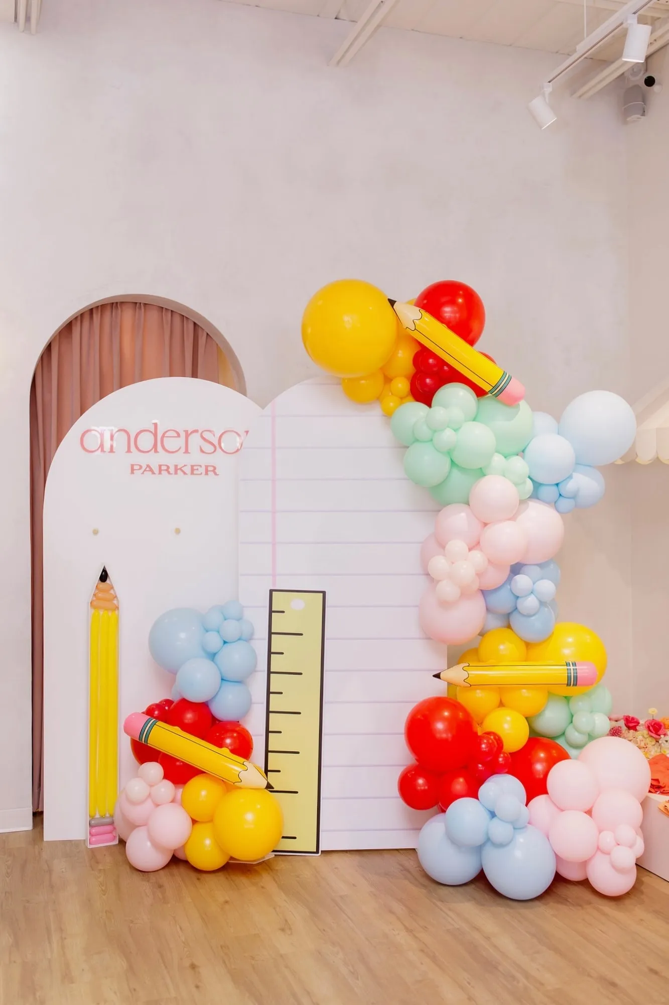 Back to school backdrop with notebook paper arch, ruler, pencil balloons and rainbow balloon garland inside the Anderson Parker boutique