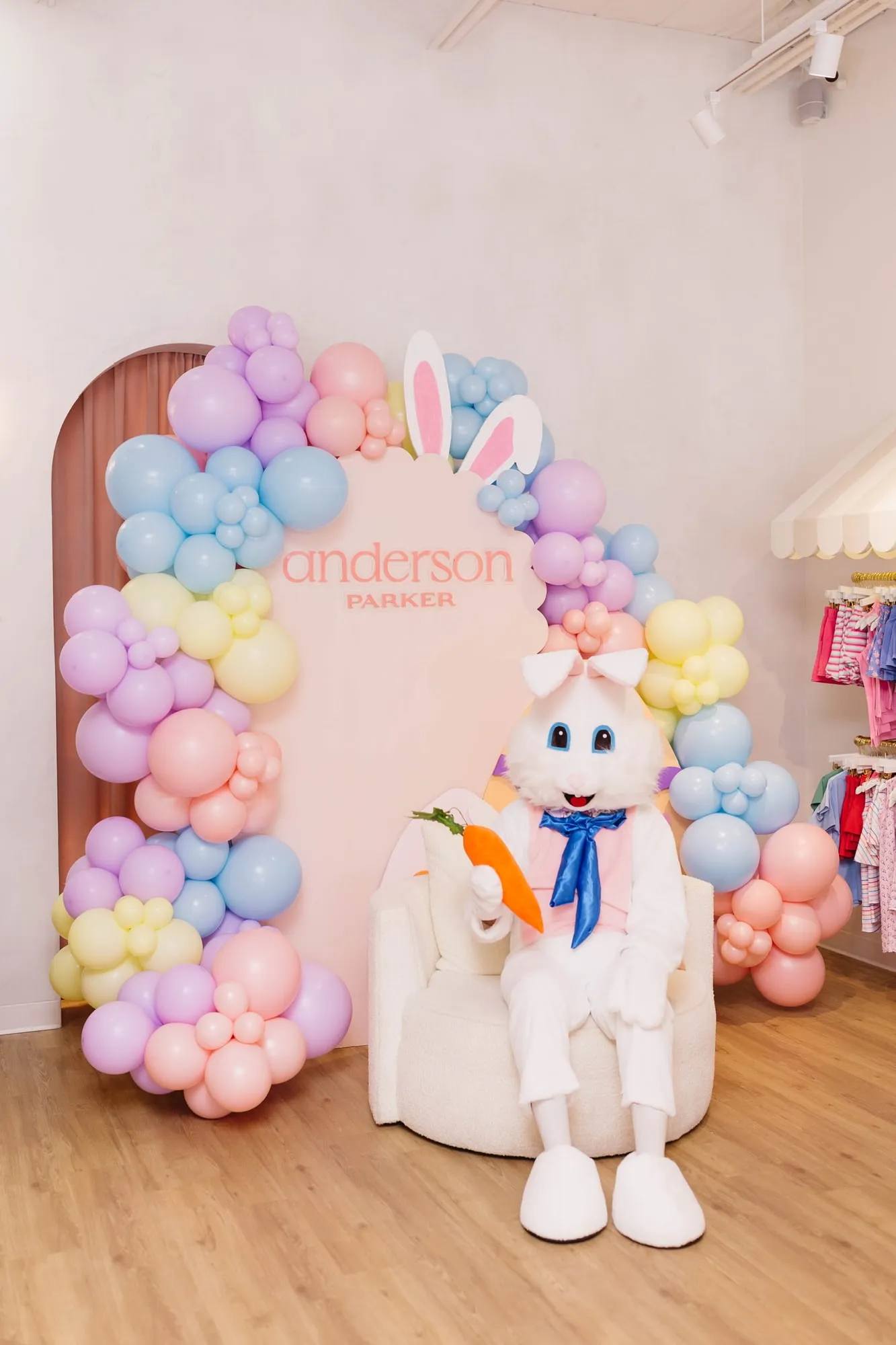 Easter event at the Anderson Parker boutique with a scalloped logo backdrop, bunny ears and pastel balloon garland