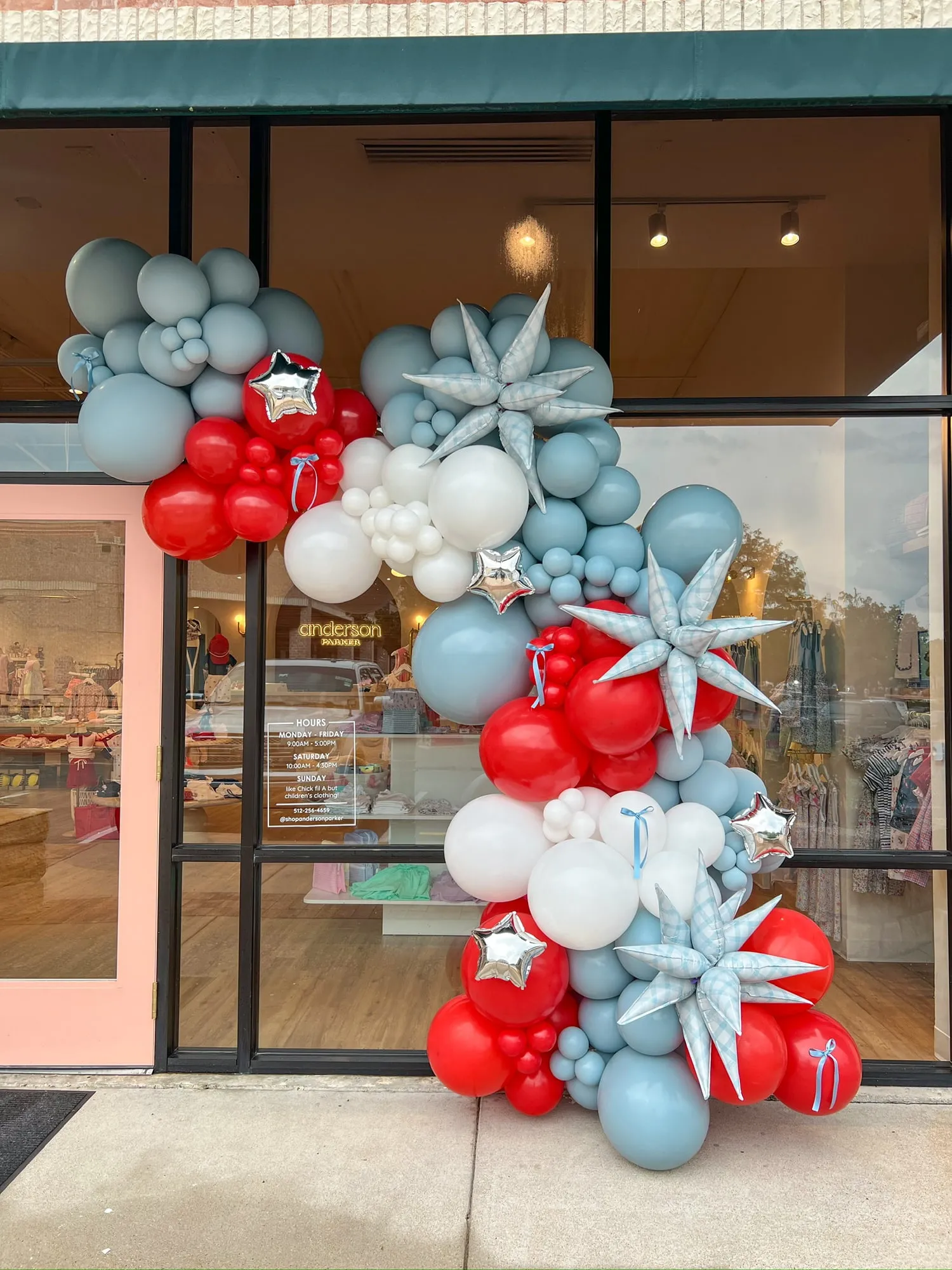 Red, white and dusty blue balloon garland with gingham starburst and silver star balloons on the Anderson Parker boutique storefront