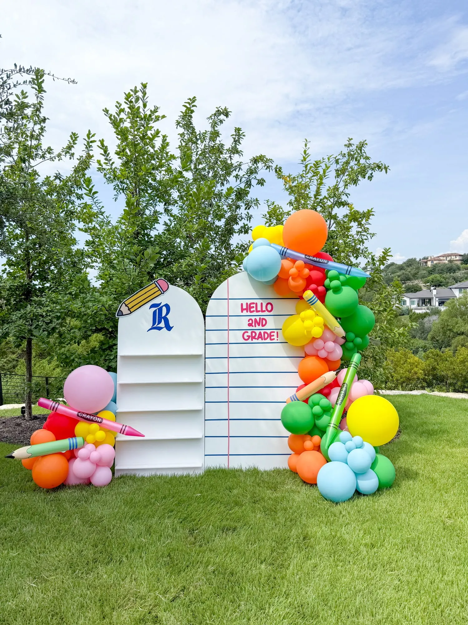 Back to school backdrop with notebook paper arch, crayon and pencil balloons and a rainbow balloon garland on a lawn