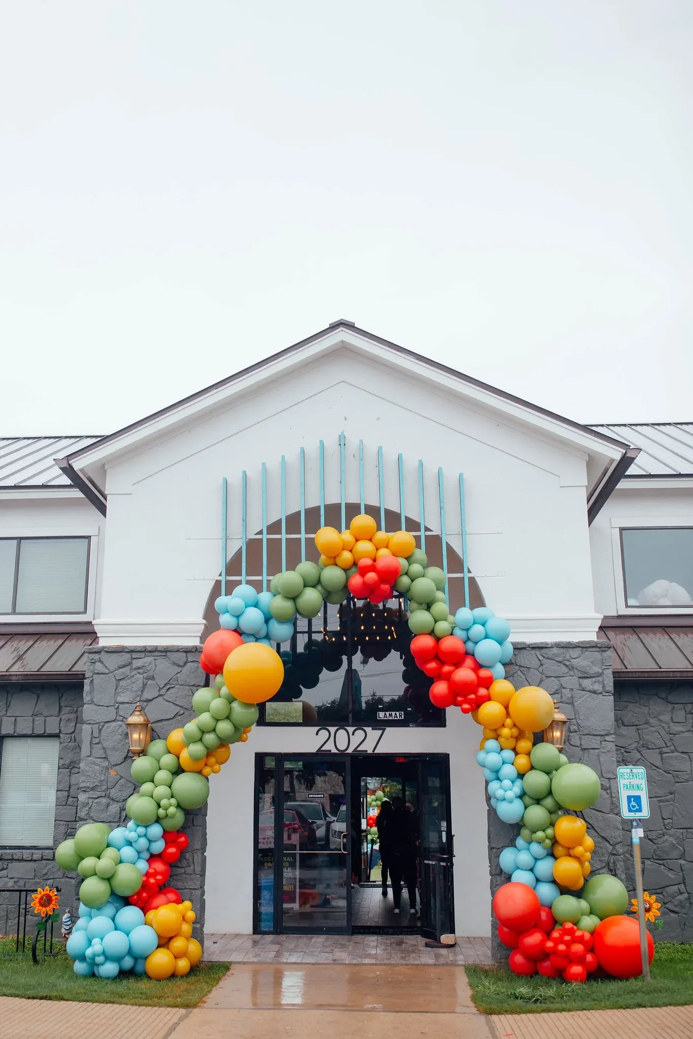 Full organic balloon arch in red, yellow, green and blue over a building entrance in Austin