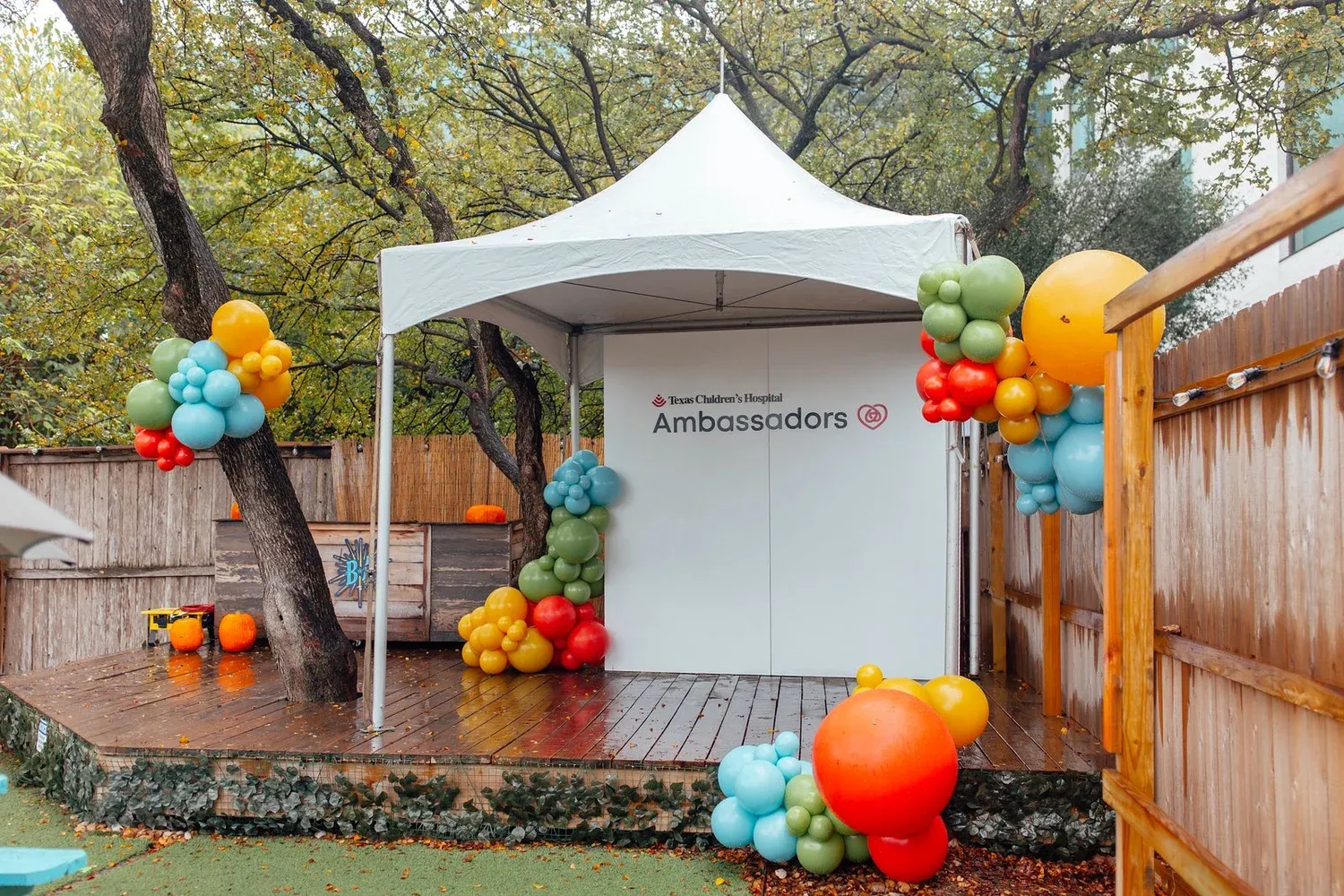 Colorful balloon clusters framing an outdoor stage and tent for a hospital ambassadors event