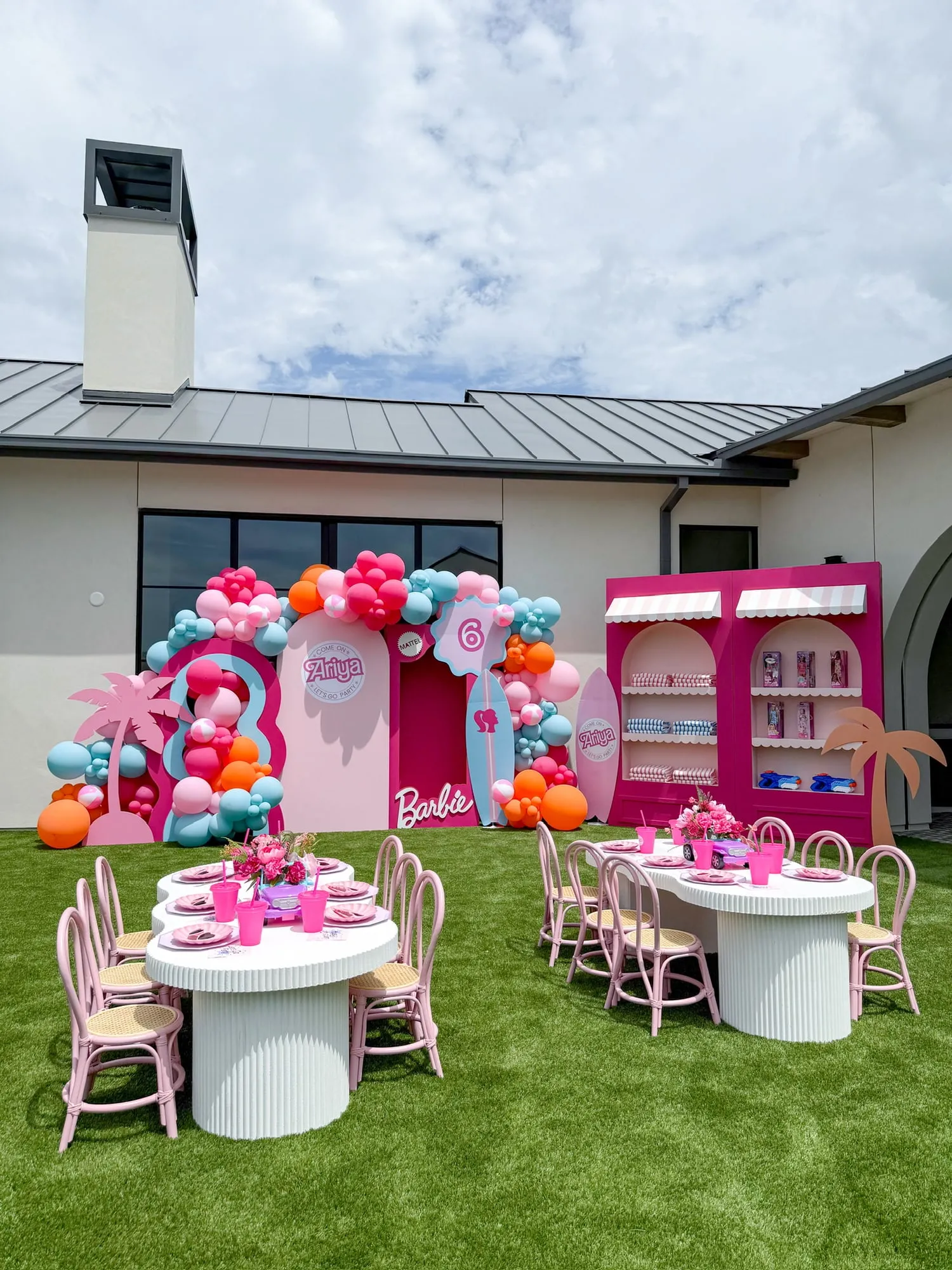 Barbie beach themed sixth birthday with pink arch backdrops, surfboards, palm tree cutouts, balloon garland and pink rattan kids tables
