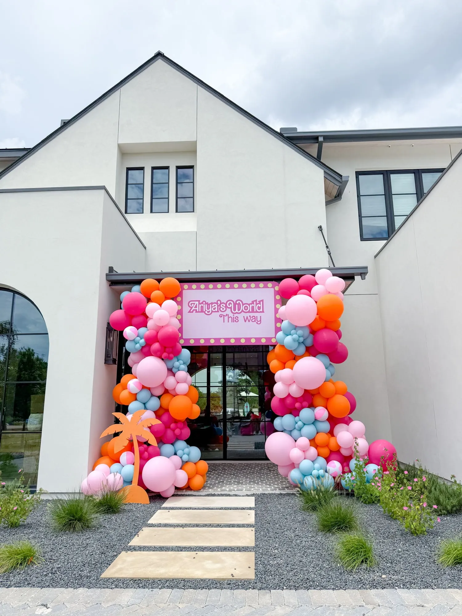 Pink, orange and blue balloon columns with beach ball balloons and a welcome sign framing a home entrance