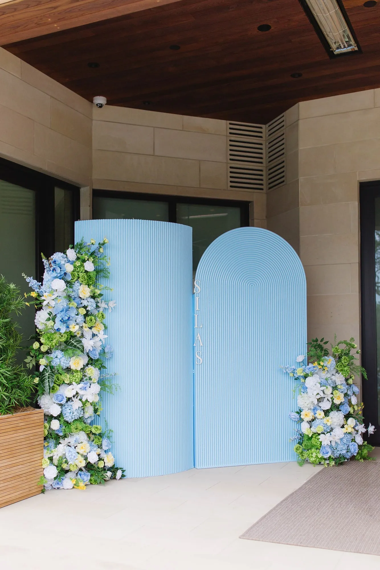 Blue fluted arch backdrops with lush blue, white and green floral installations at a covered entrance
