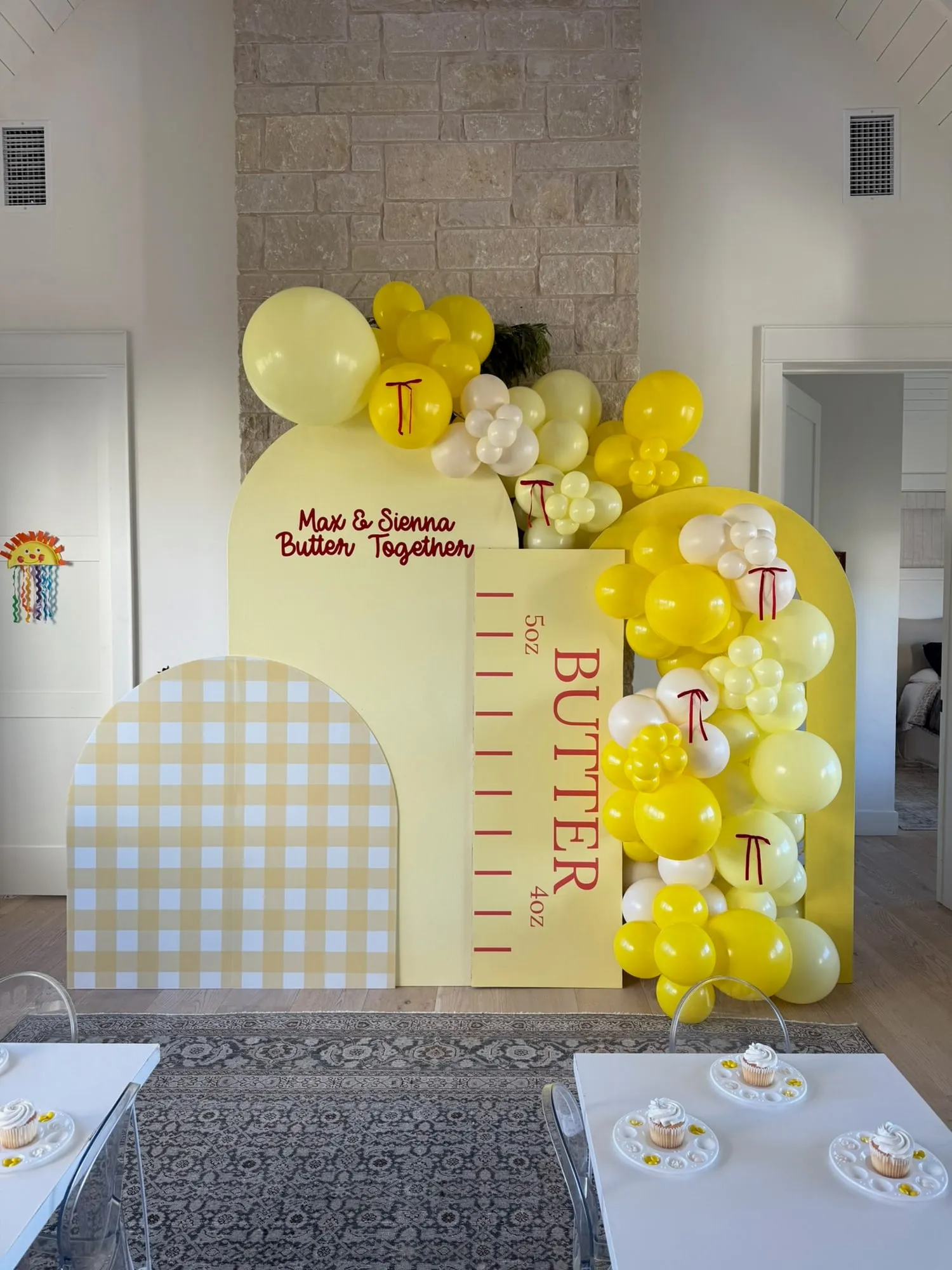 Butter themed celebration with yellow and gingham arch backdrops, a butter stick panel and yellow balloon garland with red bows