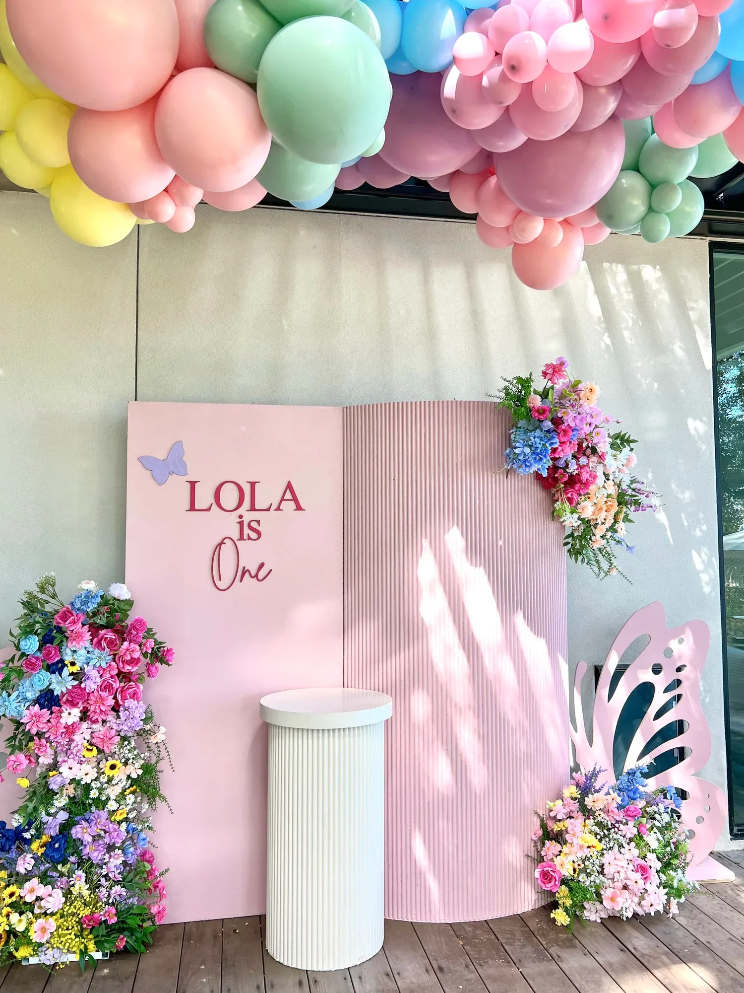 Butterfly first birthday with pink fluted backdrop, custom name sign, florals and pastel balloon garland