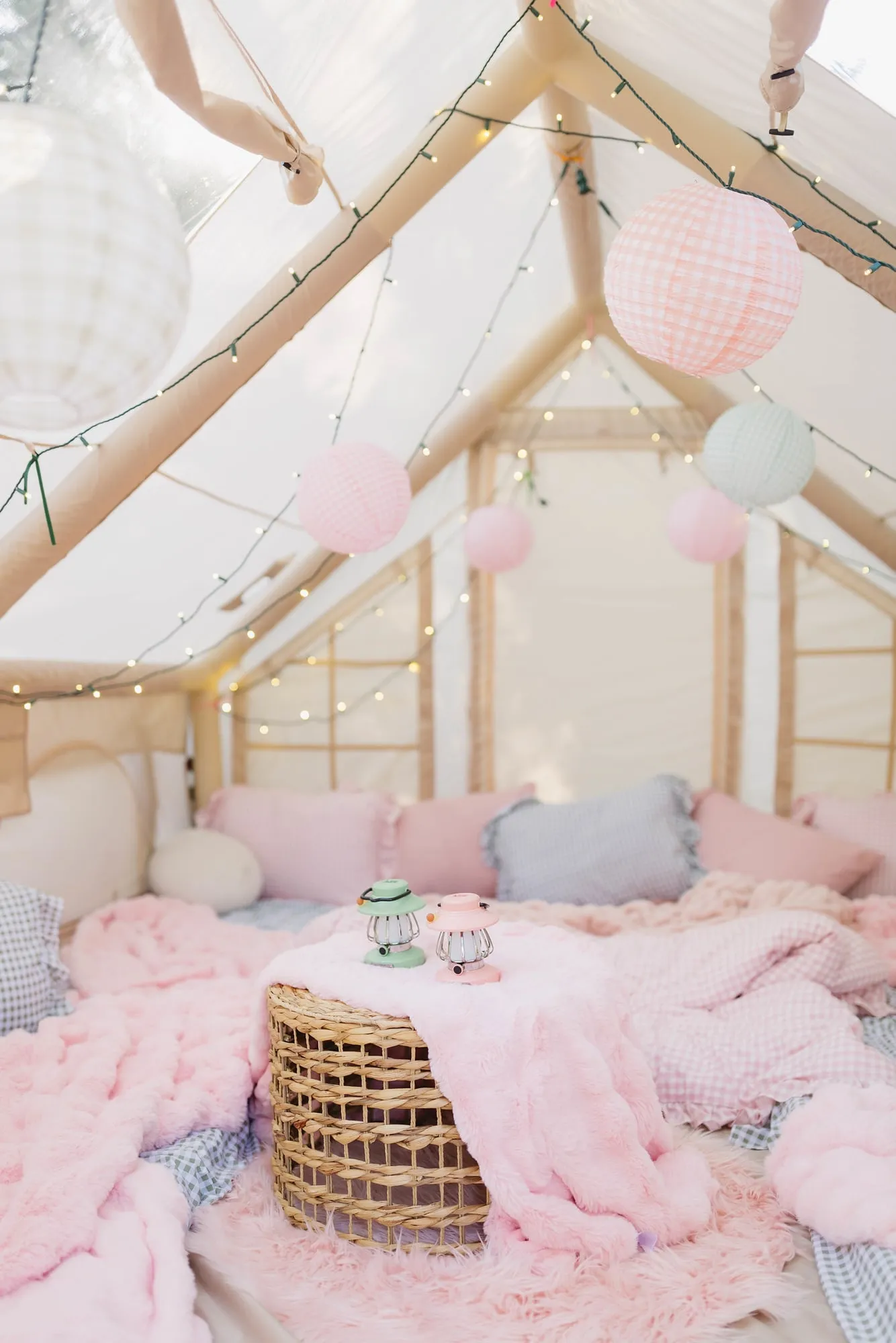 Glamping tent sleepover interior with pink faux fur, gingham bedding, paper lanterns and twinkle lights