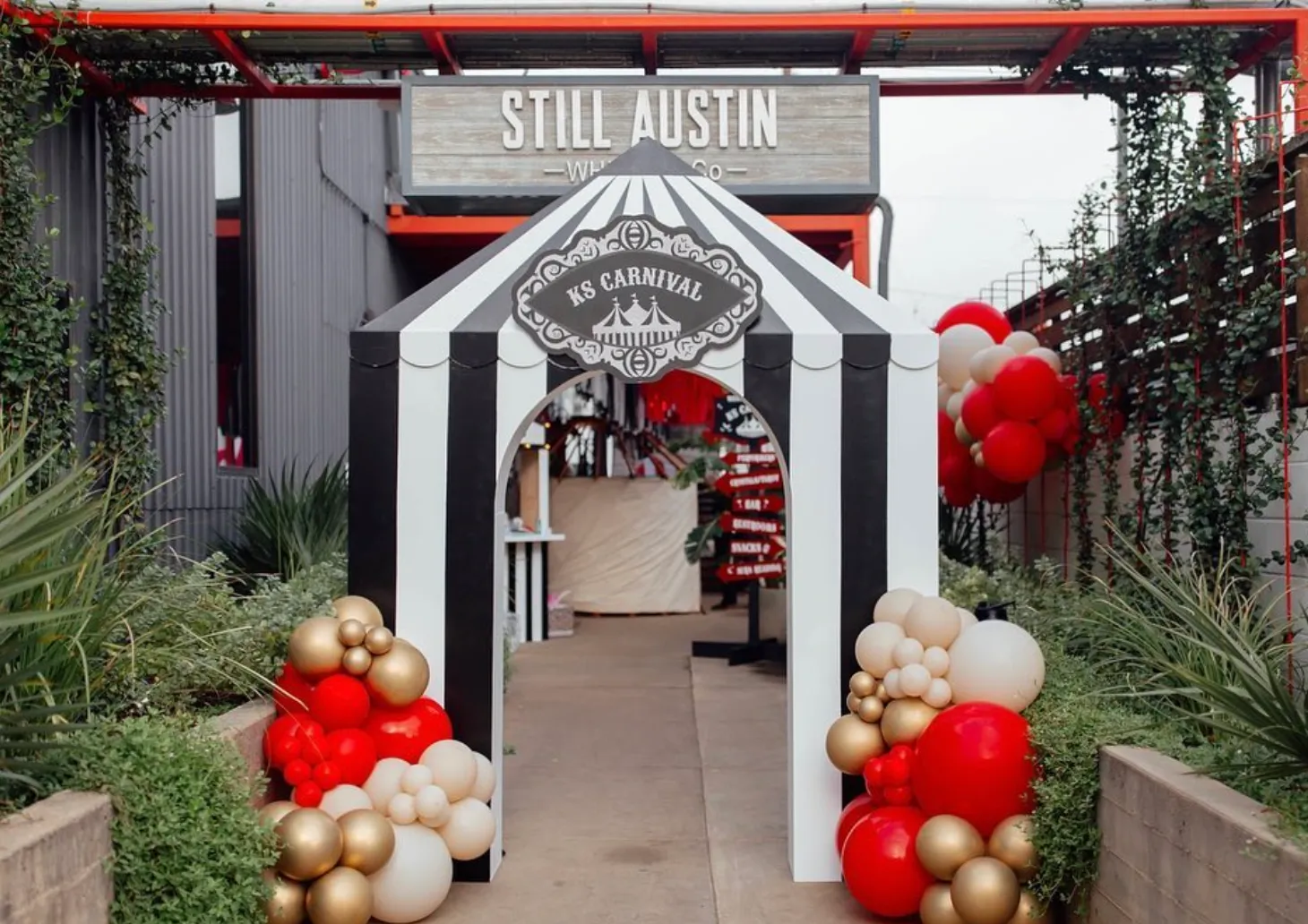 Striped carnival tent entrance arch with red, cream and gold balloon clusters at Still Austin