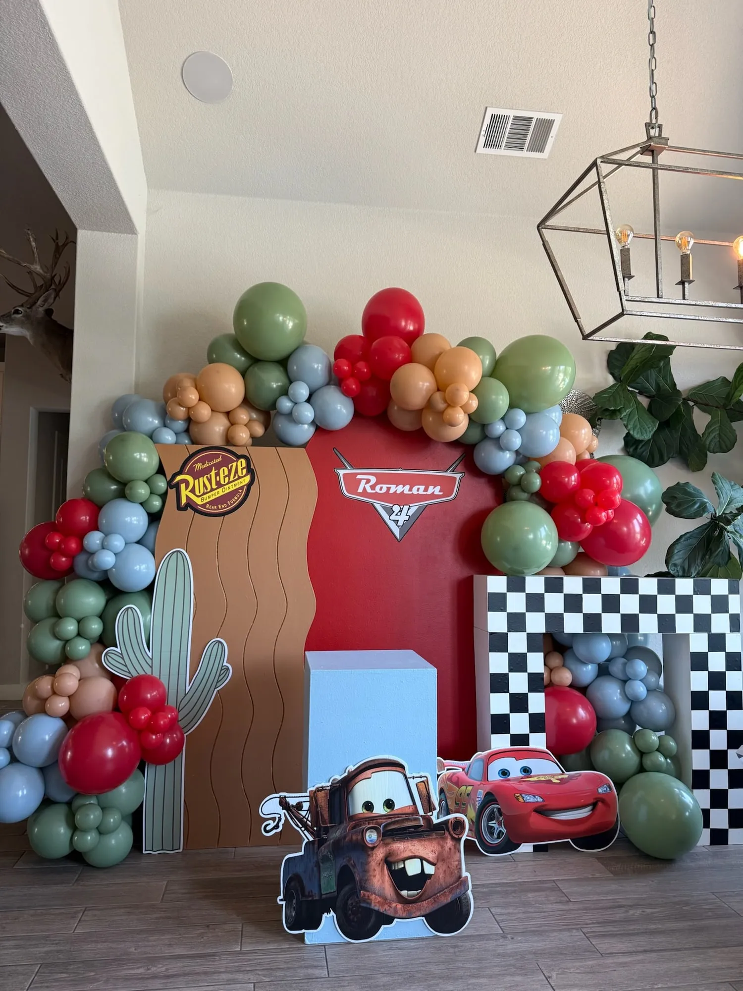 Cars themed fourth birthday with a red and desert backdrop, checkered finish line, cactus cutout and red, sage, tan and slate balloon garland
