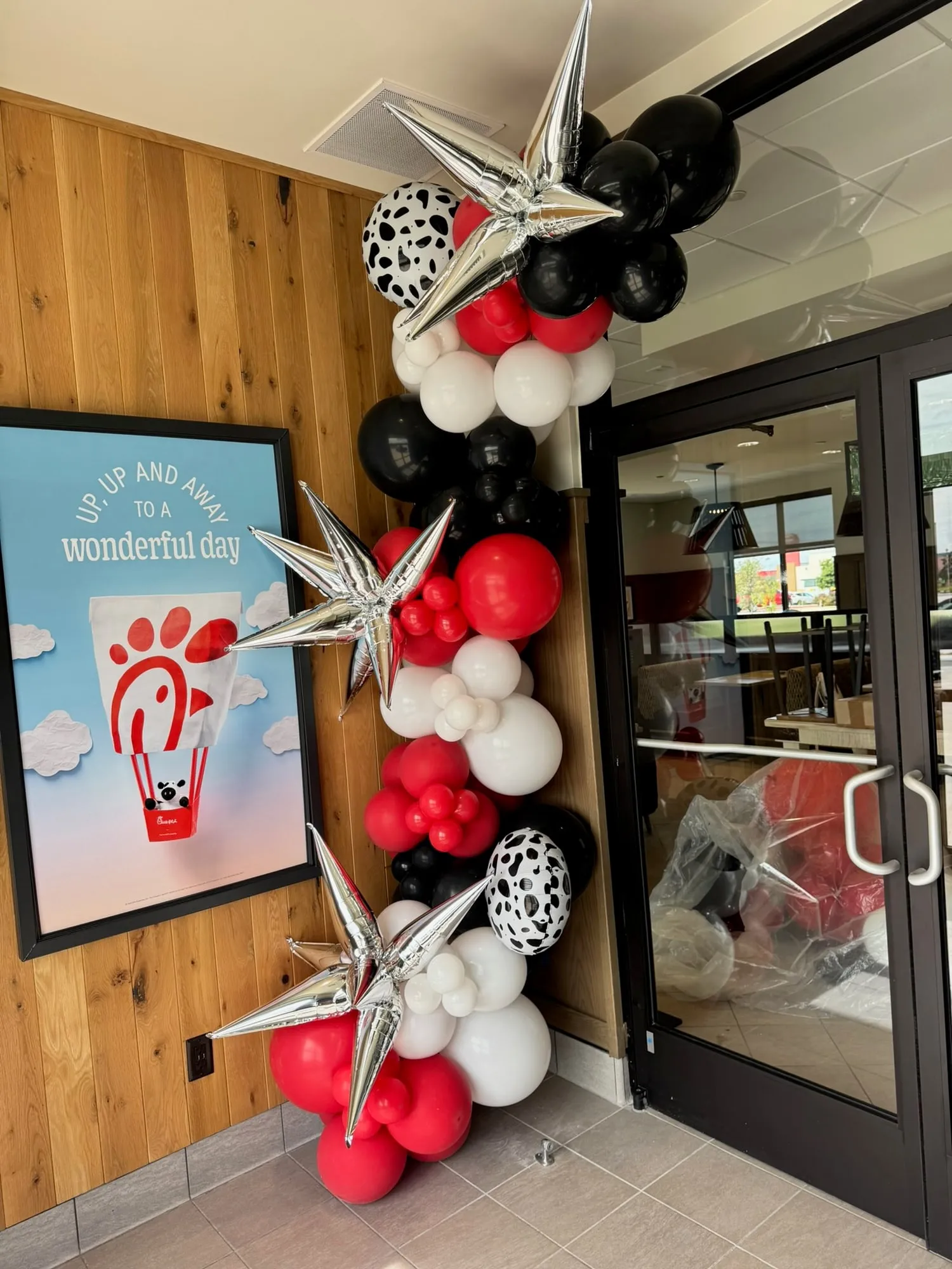 Red, white and black balloon garland with cow print and silver starburst balloons at a Chick-fil-A restaurant entrance