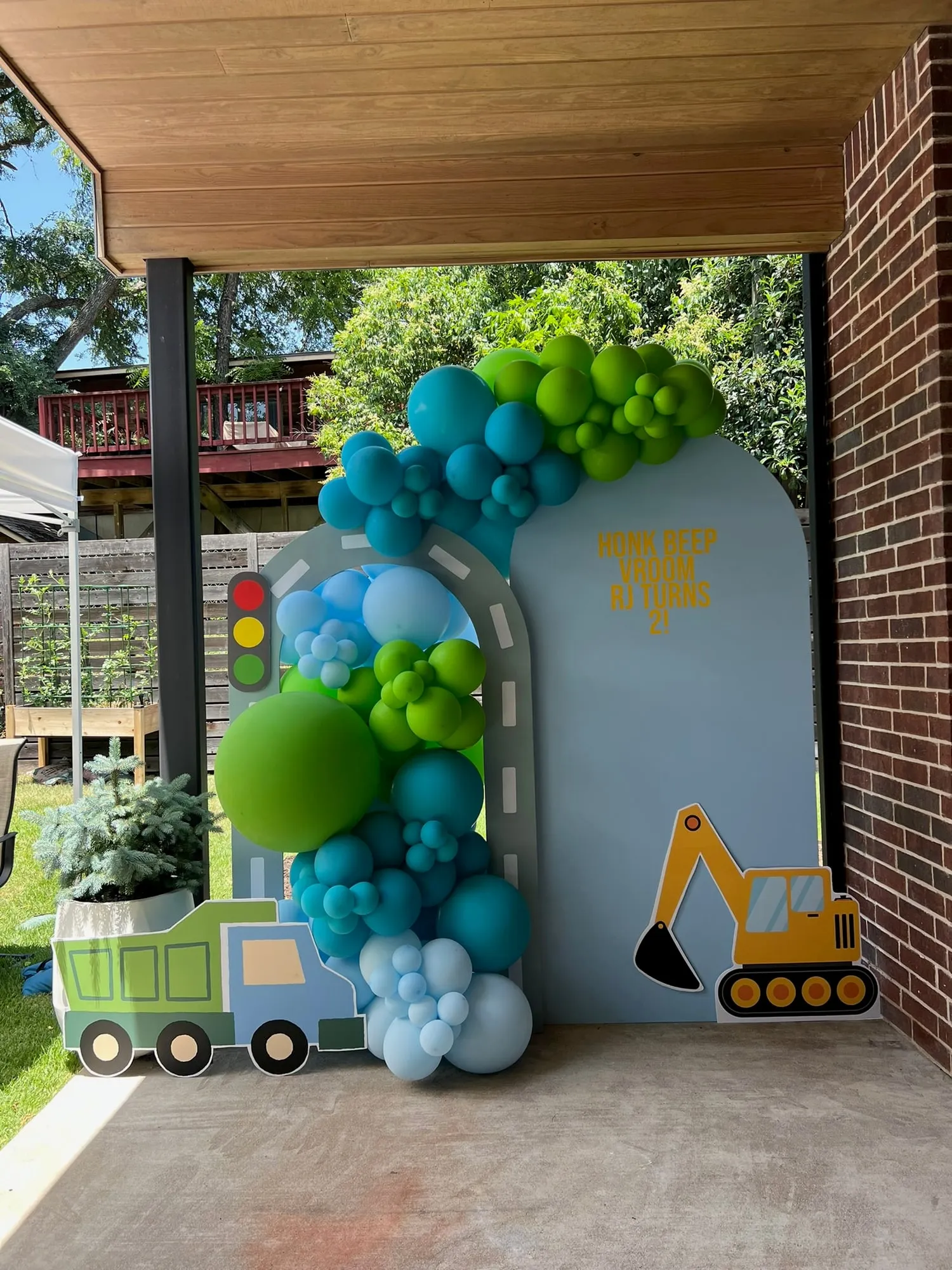Construction themed second birthday with a road arch backdrop, teal, lime and blue balloon garland, dump truck and excavator cutouts