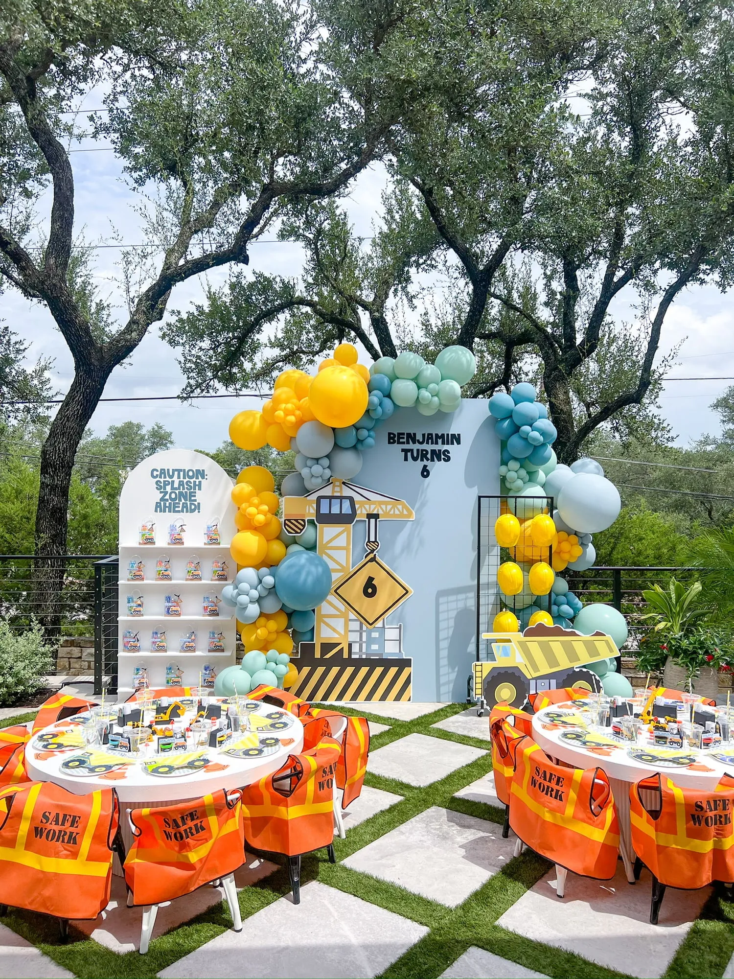 Construction themed sixth birthday with crane backdrop, yellow and teal balloon garland, hard hat wall and kids tables with safety vests