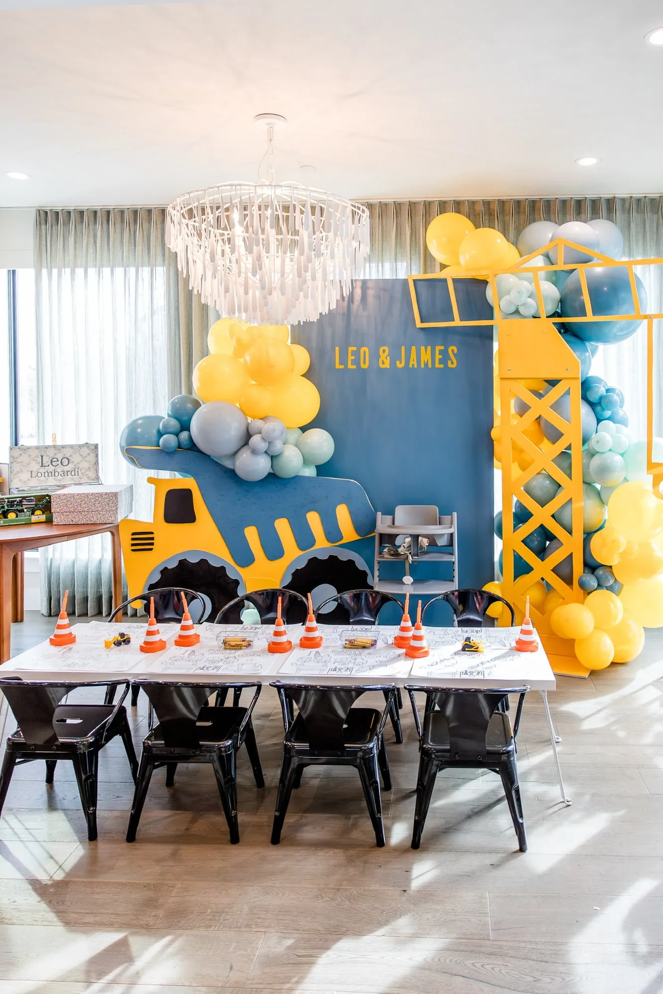 Construction themed twins birthday with a dump truck and crane backdrop, yellow and blue balloon garland and a styled kids table