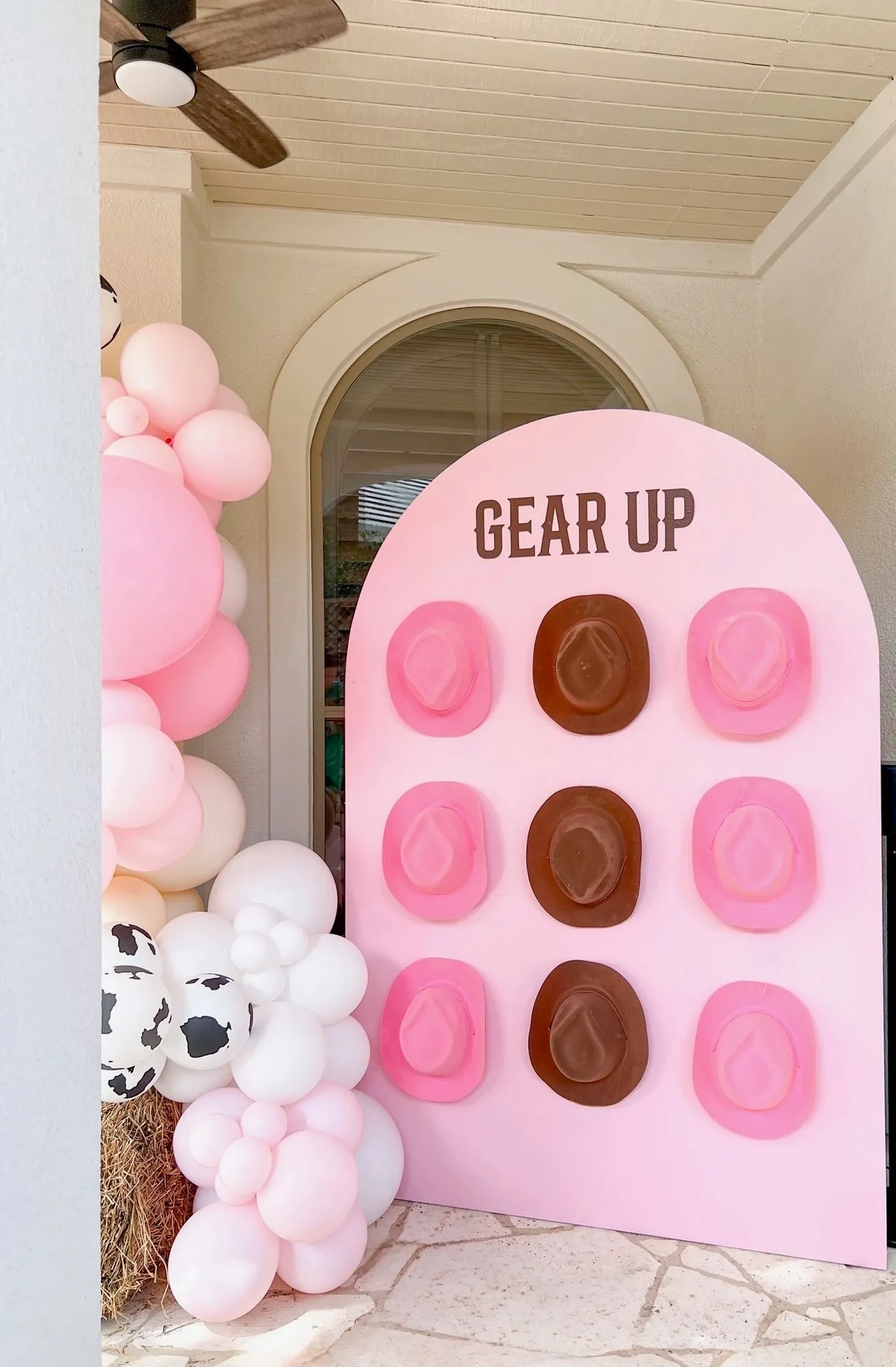 Pink arch Gear Up wall with cowboy hats beside a pink, white and cow print balloon garland