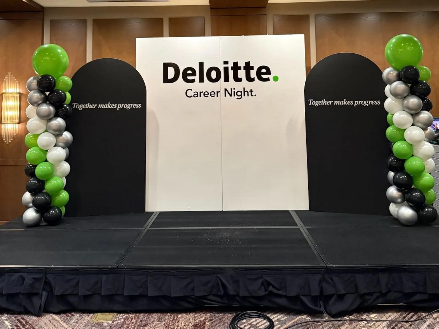 Deloitte Career Night stage with a branded white backdrop, black arch panels and green, black, silver and white balloon columns