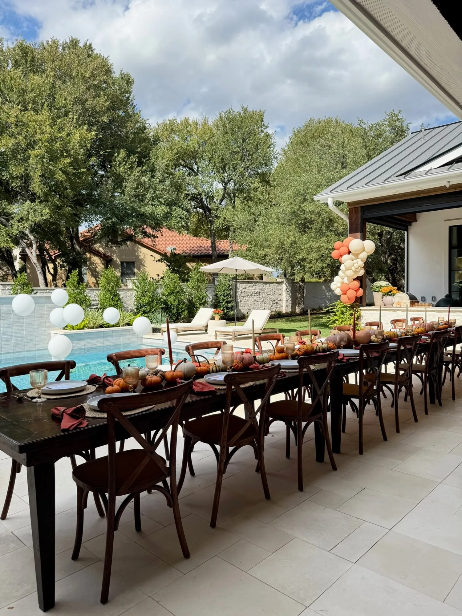Poolside fall baby shower with a long wooden harvest table, pumpkin centerpieces and terracotta and cream balloon columns
