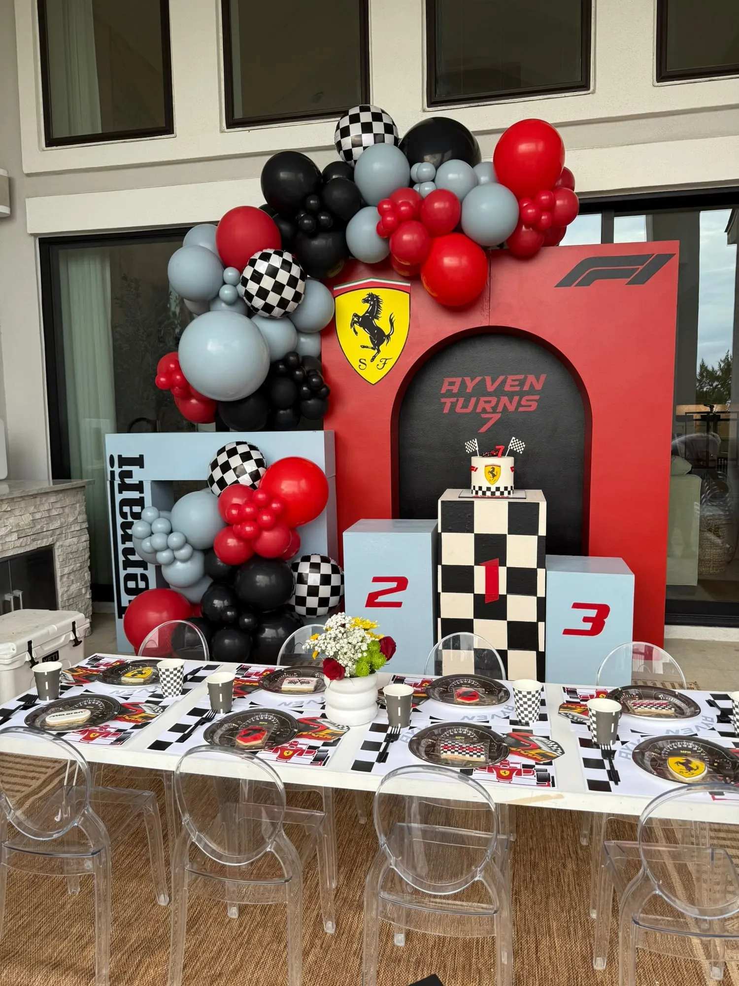Formula 1 themed seventh birthday with a red race backdrop, winners podium, checkered balloon garland and a styled kids table