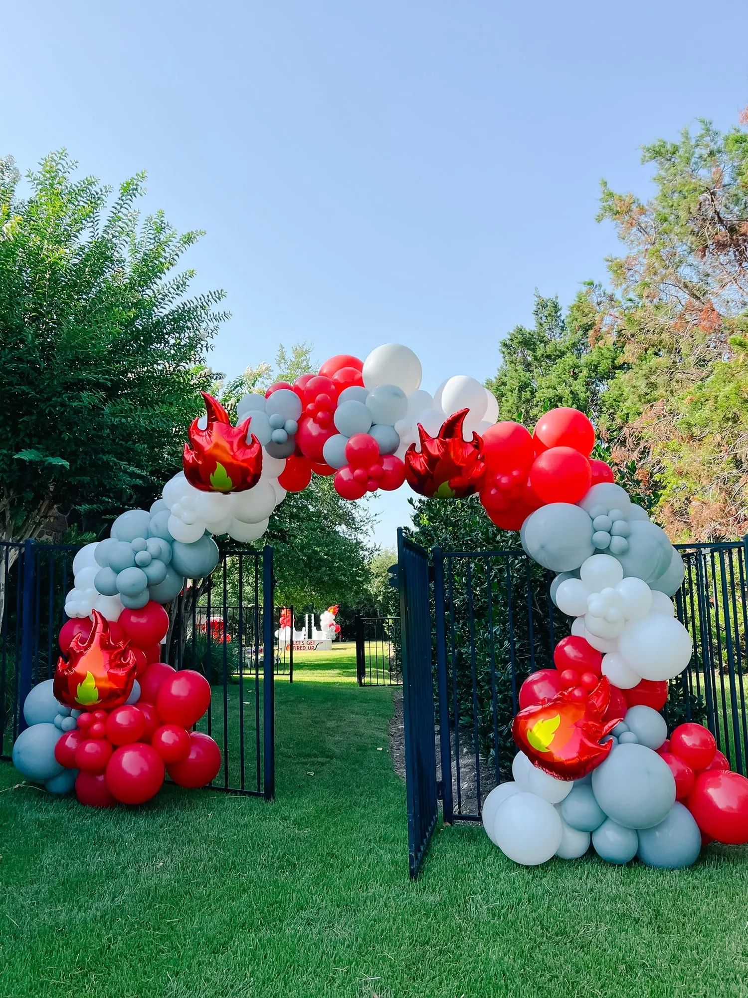 Red, white and gray balloon arch with flame balloons framing a backyard gate for a firefighter themed party