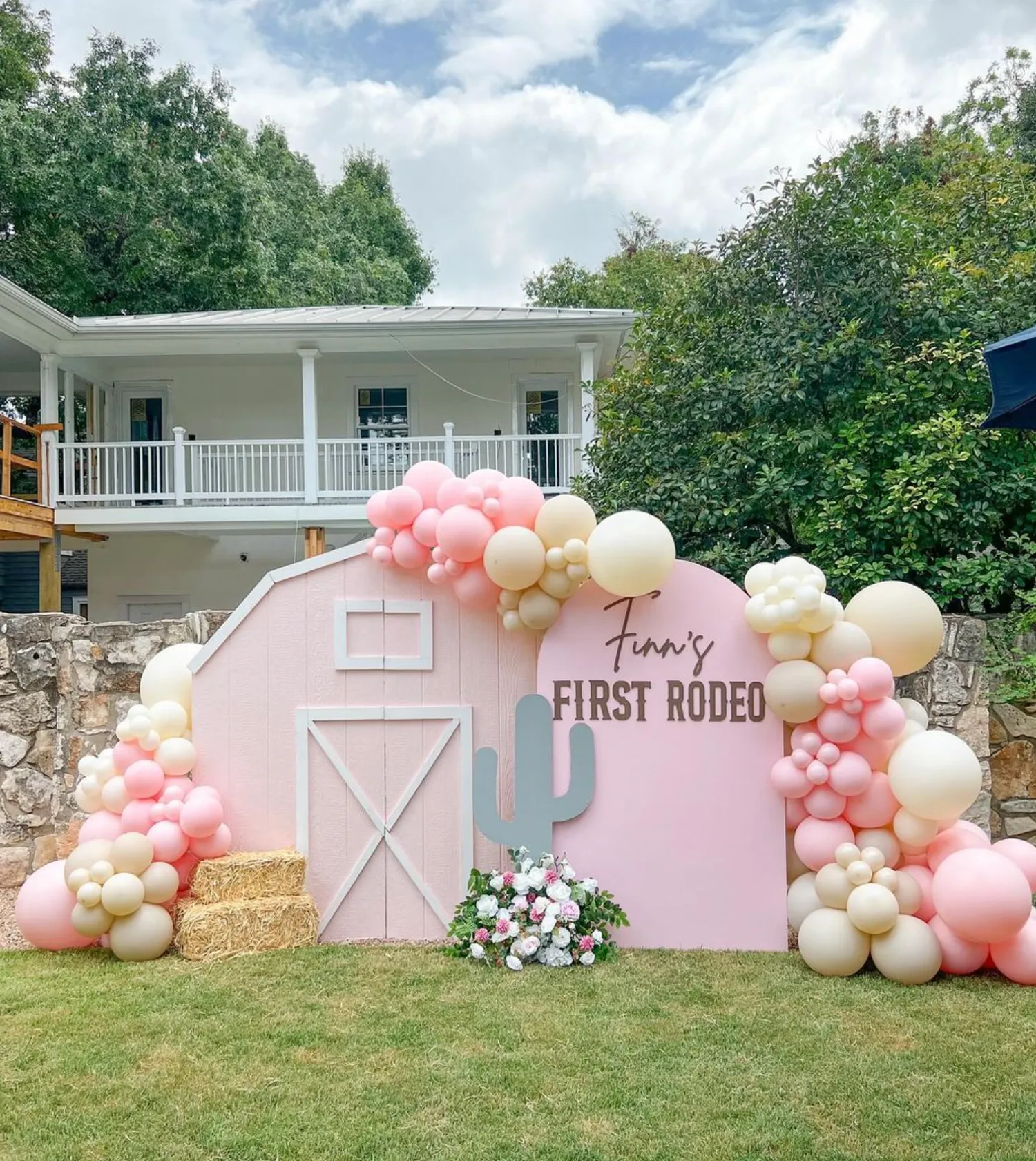 First rodeo birthday with pink barn backdrop, arch sign, hay bales and blush balloon garland