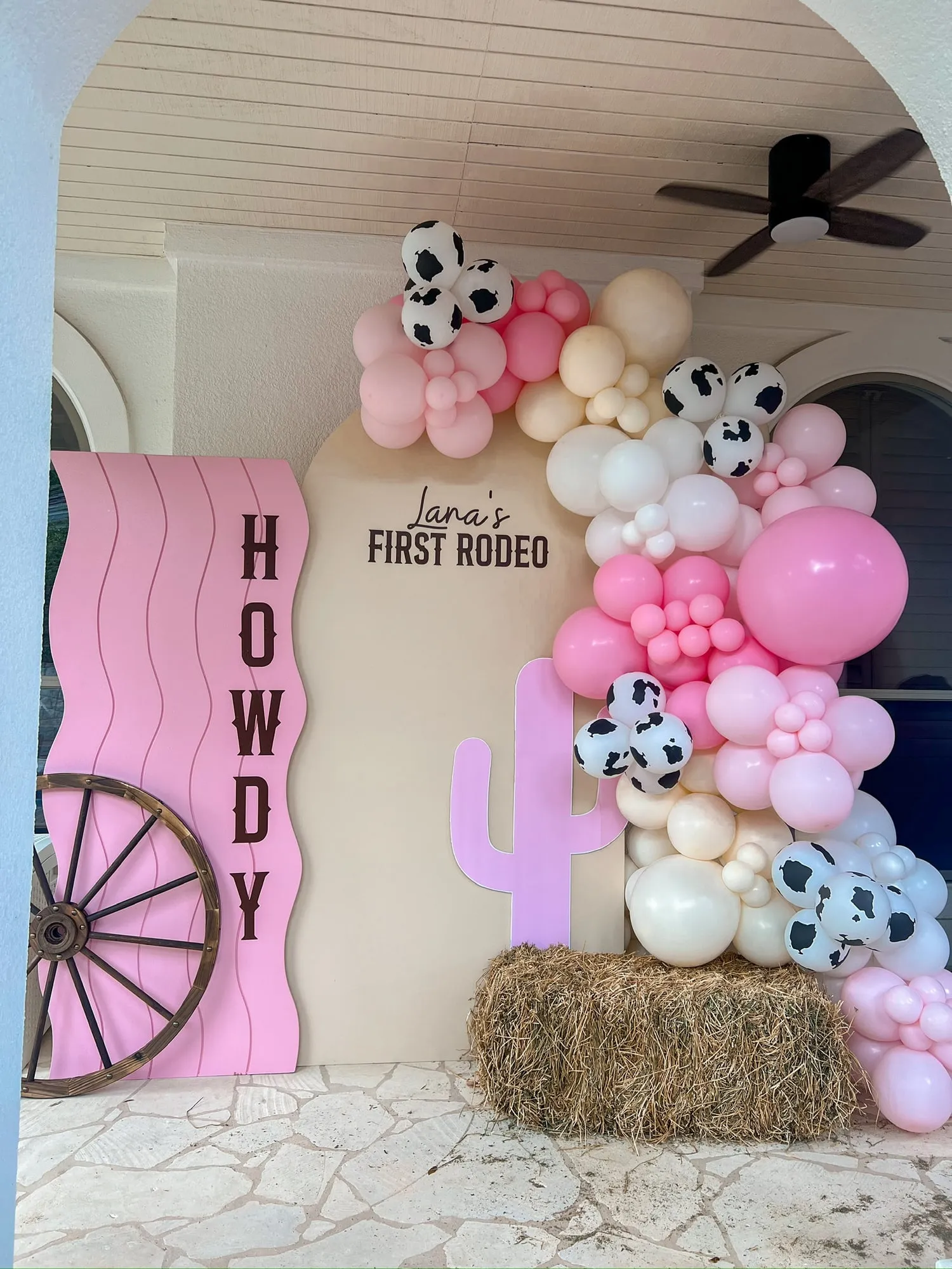 First rodeo birthday with a pink wavy Howdy panel, cactus cutout, hay bale and pink and cow print balloon garland