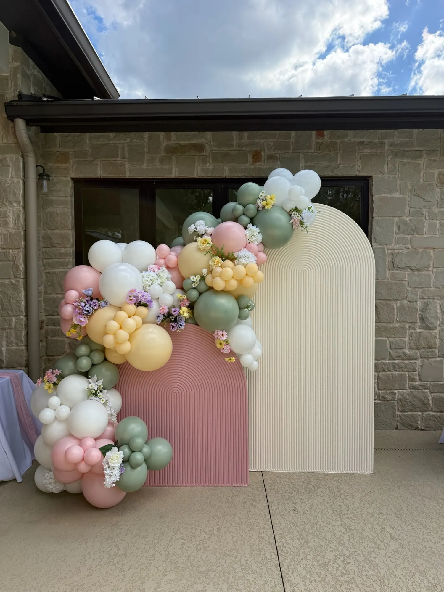 Dusty pink and cream fluted arches with a pastel balloon garland woven with spring florals
