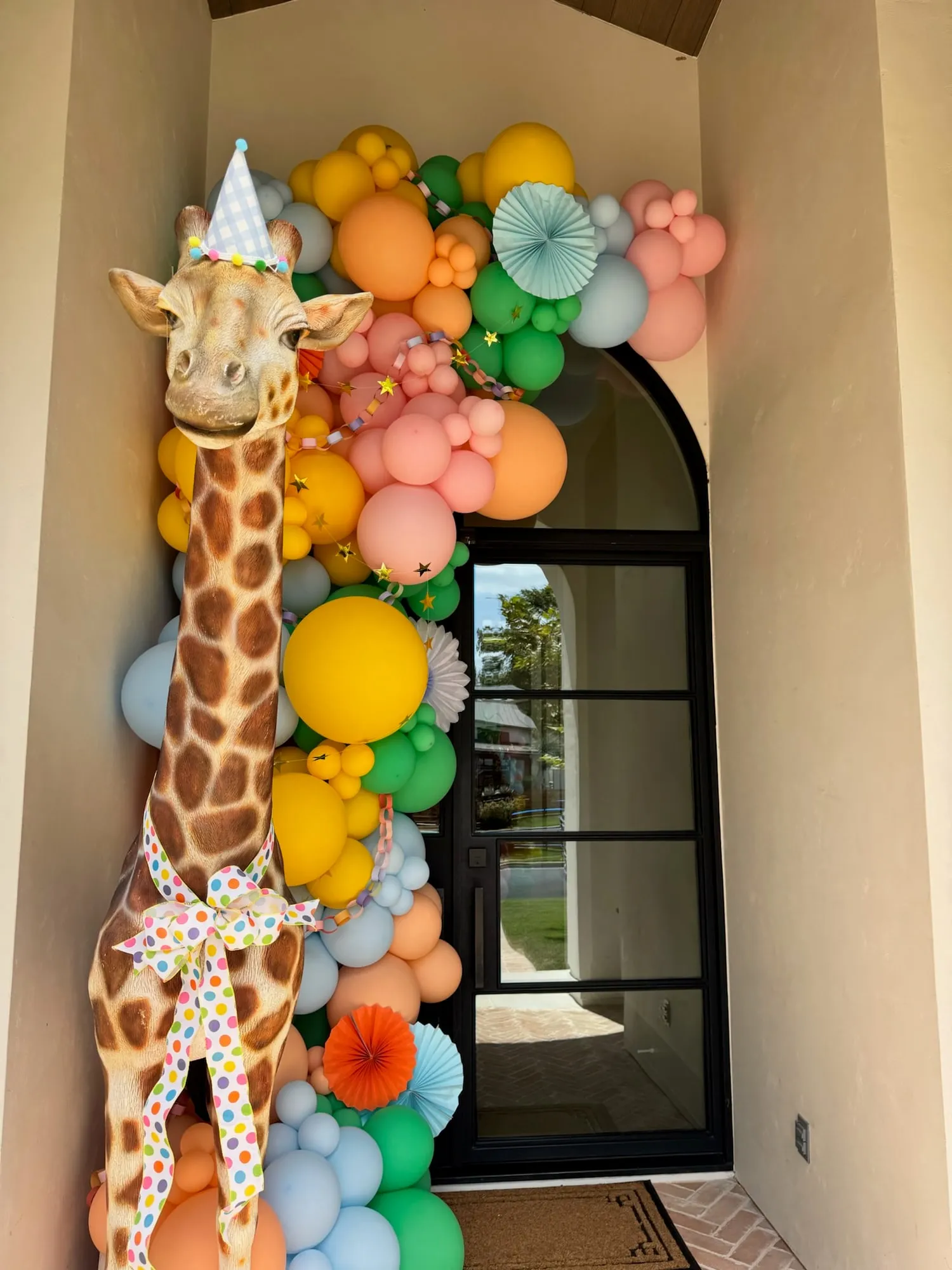 Party animals front door balloon garland in rainbow pastels with paper fans, star garland and a giraffe in a party hat
