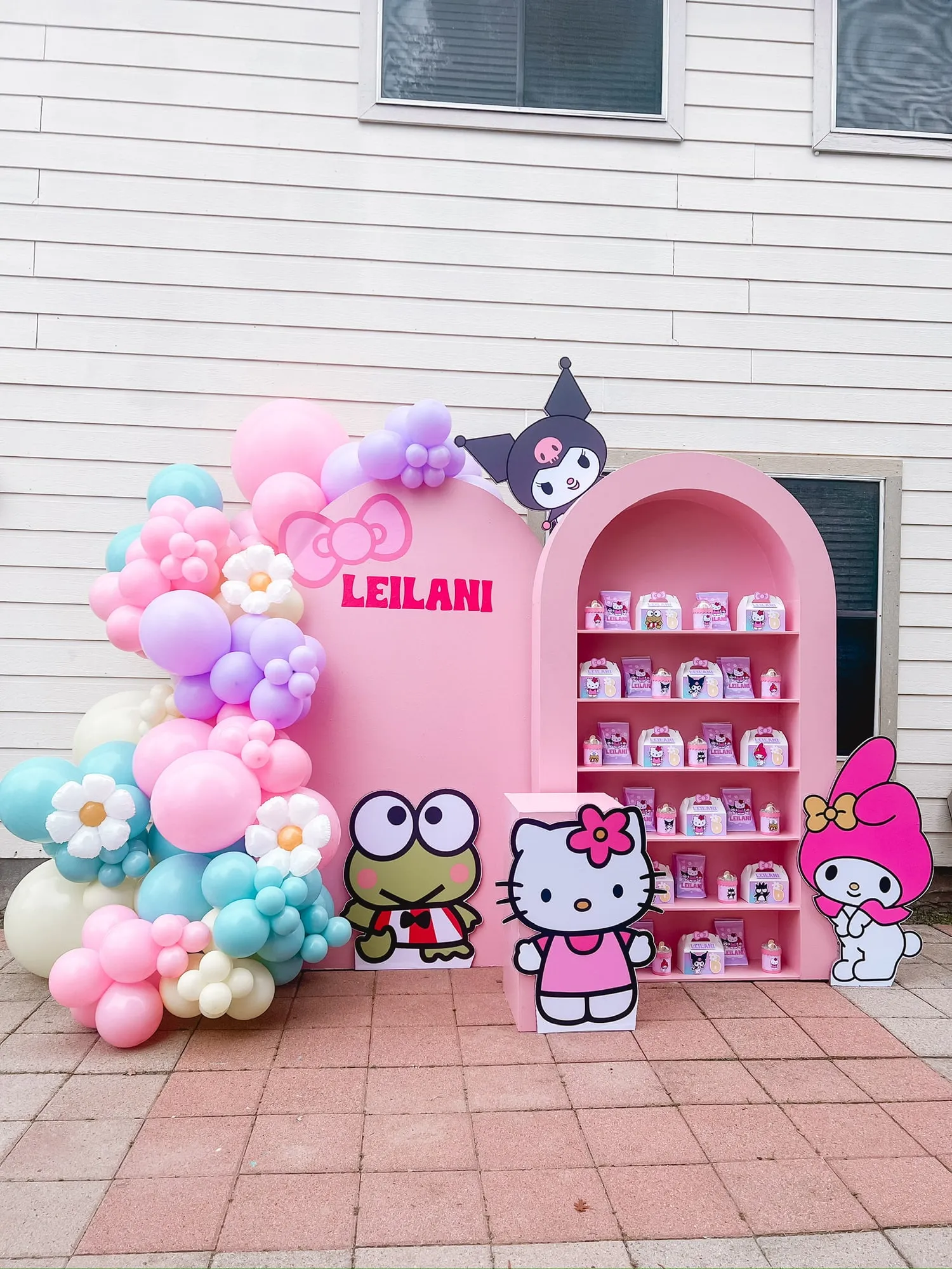 Hello Kitty themed birthday with a pink arch backdrop, pastel balloon garland with daisy balloons and a favor shelf