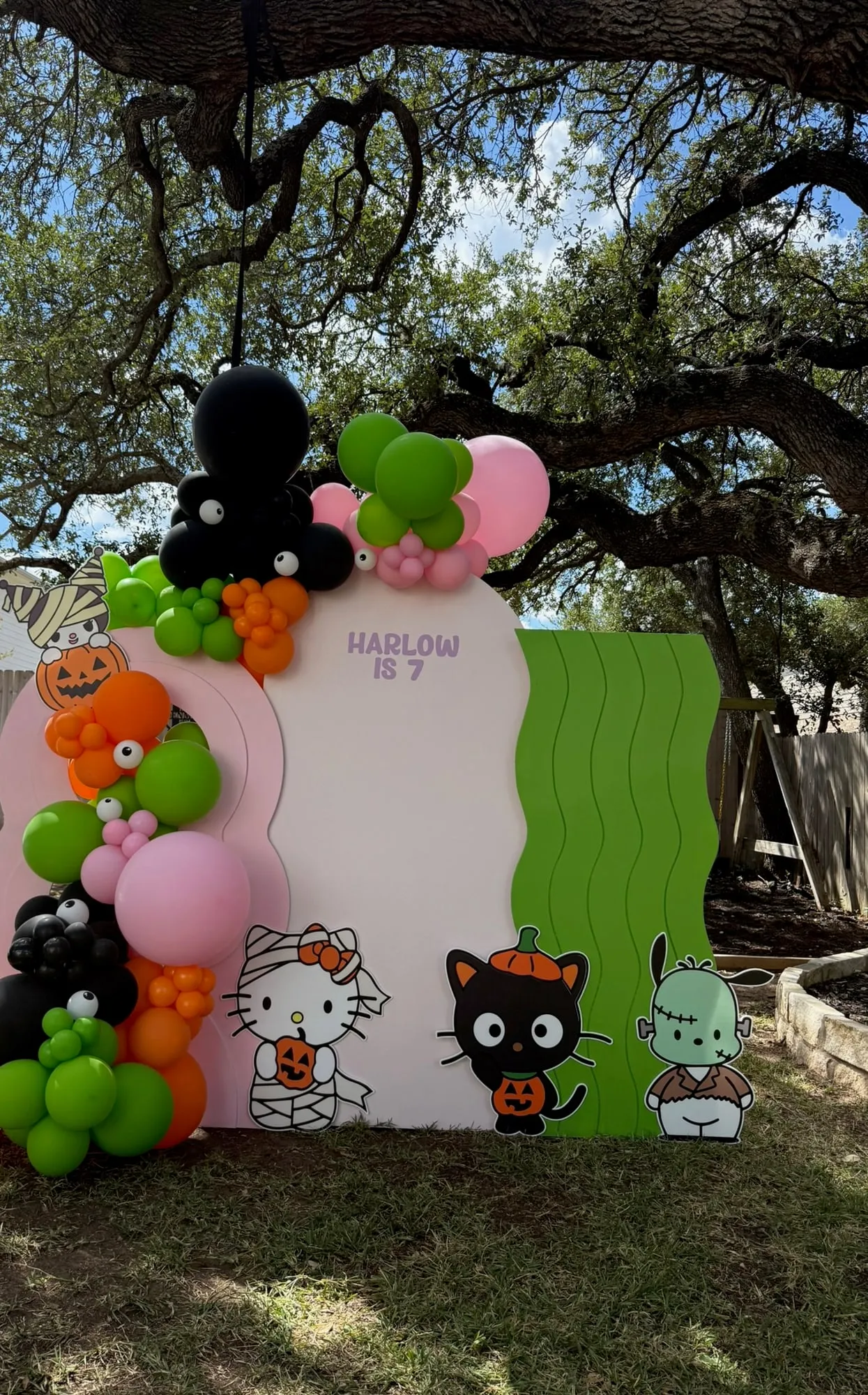 Hello Kitty Halloween seventh birthday with pink, cream and green wavy panels, character cutouts and orange, green and black balloons