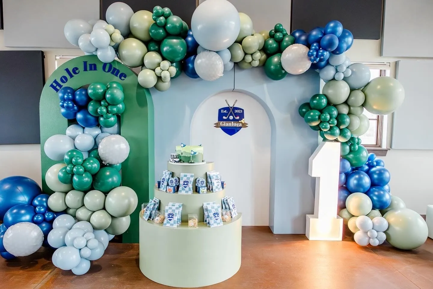 Hole in one golf themed first birthday with a green, blue and sage organic balloon garland, golf ball balloons, arch backdrops and a lighted number 1
