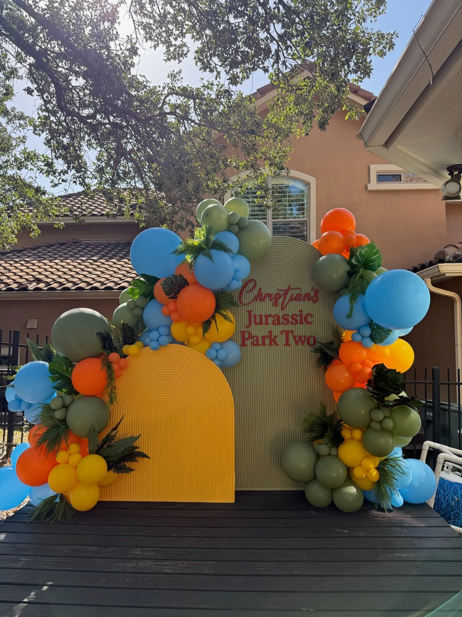 Jurassic themed second birthday with mustard and sage fluted arches, tropical greenery and orange, blue, yellow and olive balloon garland