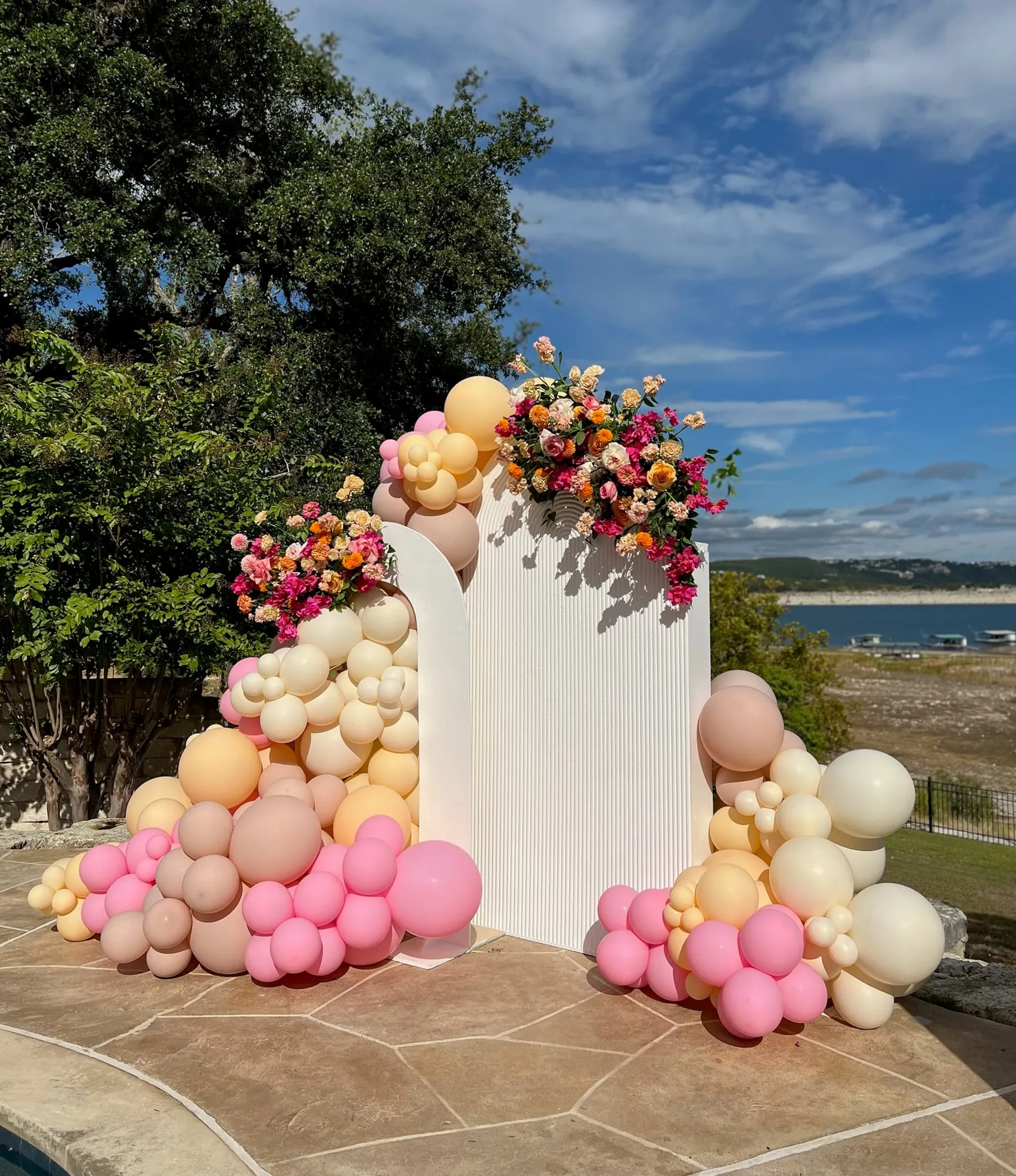 White fluted arch backdrops with pink, peach and cream balloons and fresh florals overlooking Lake Travis