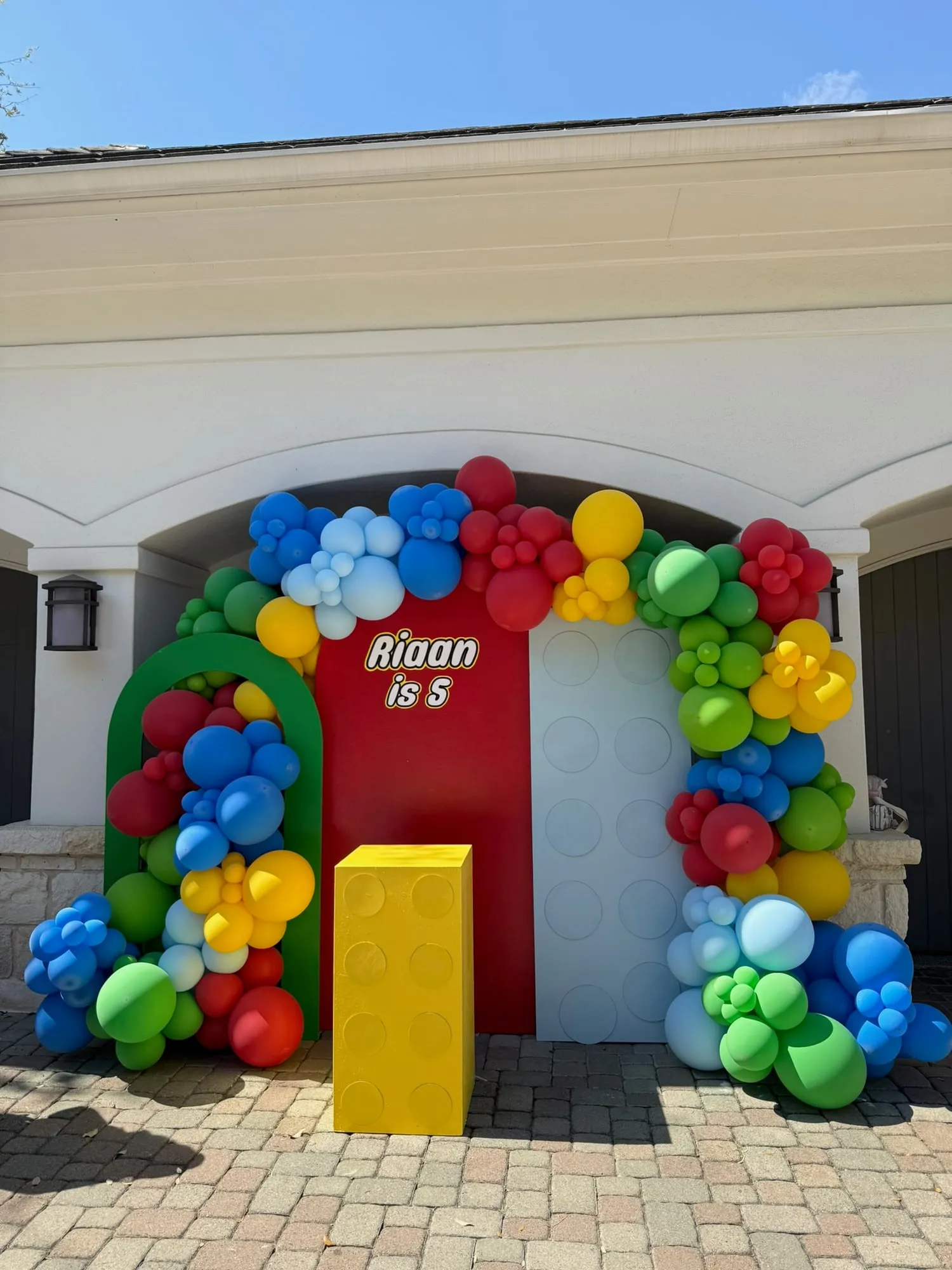 Building block themed fifth birthday with red, green and white panels, a yellow brick pedestal and a primary color balloon arch