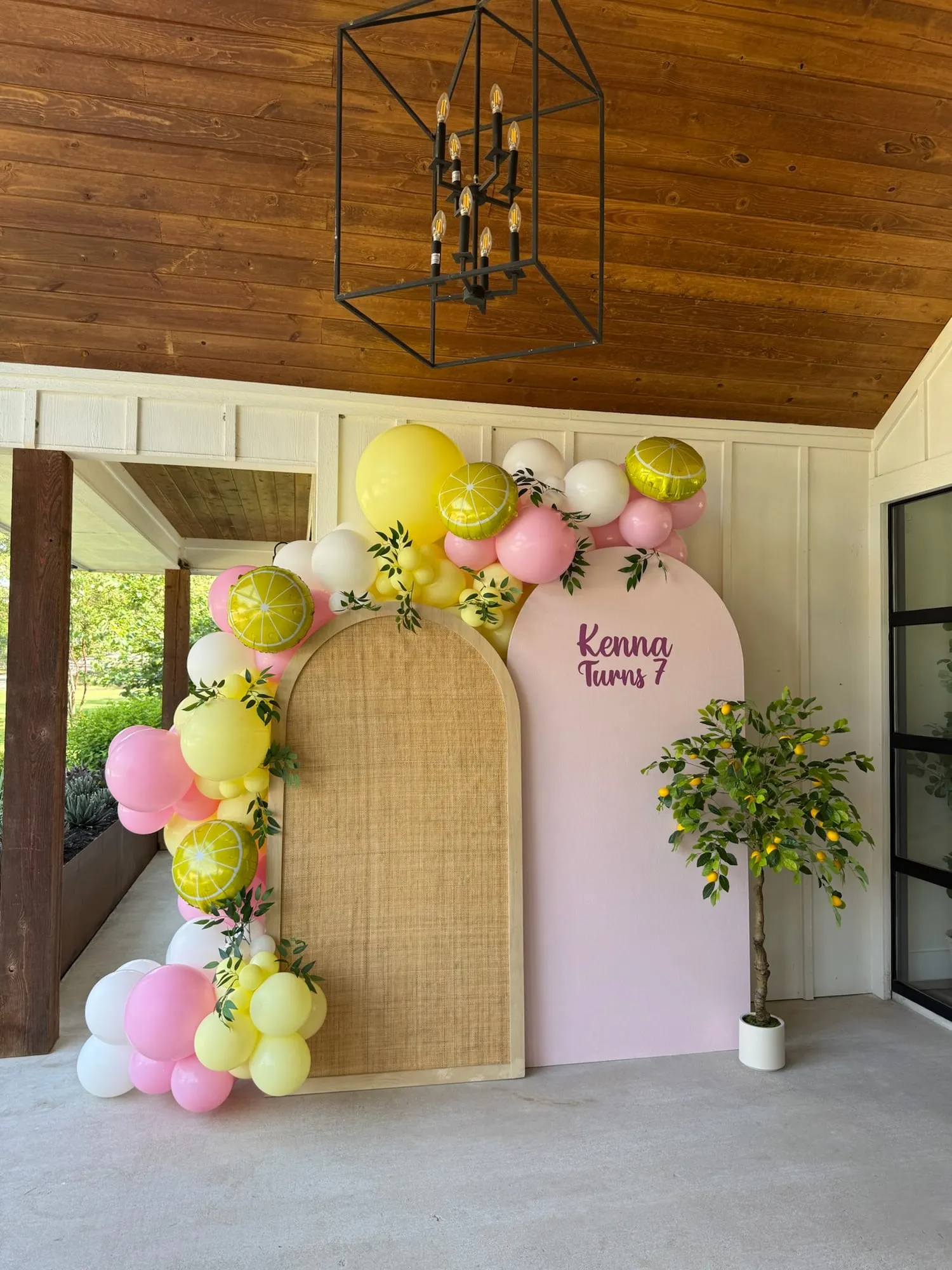 Lemonade themed seventh birthday with rattan and pink arches, lemon slice balloons, greenery and a lemon tree on a porch