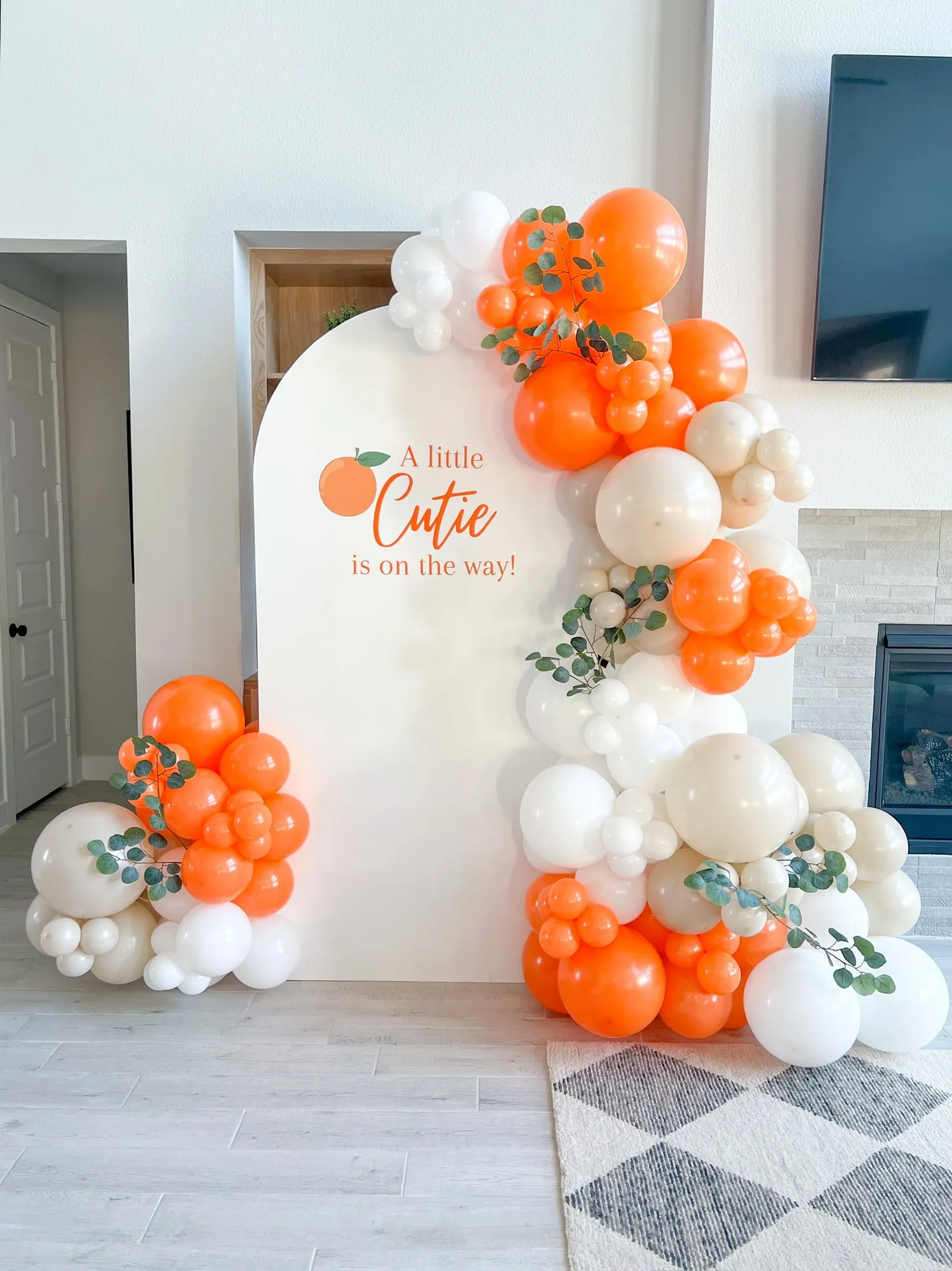 Little Cutie baby shower with a white arch backdrop, orange, white and sand balloon garland and eucalyptus