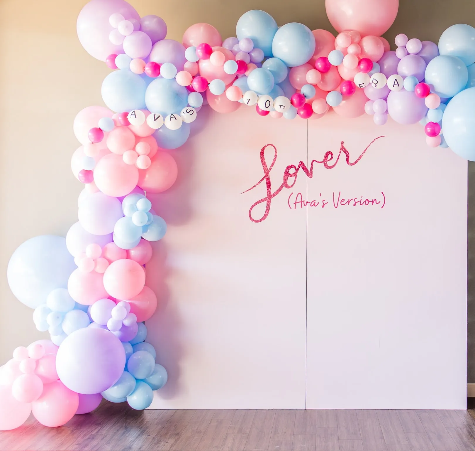 Lover era tenth birthday backdrop with a pink script sign and a pastel pink, lilac and blue balloon garland with letter beads