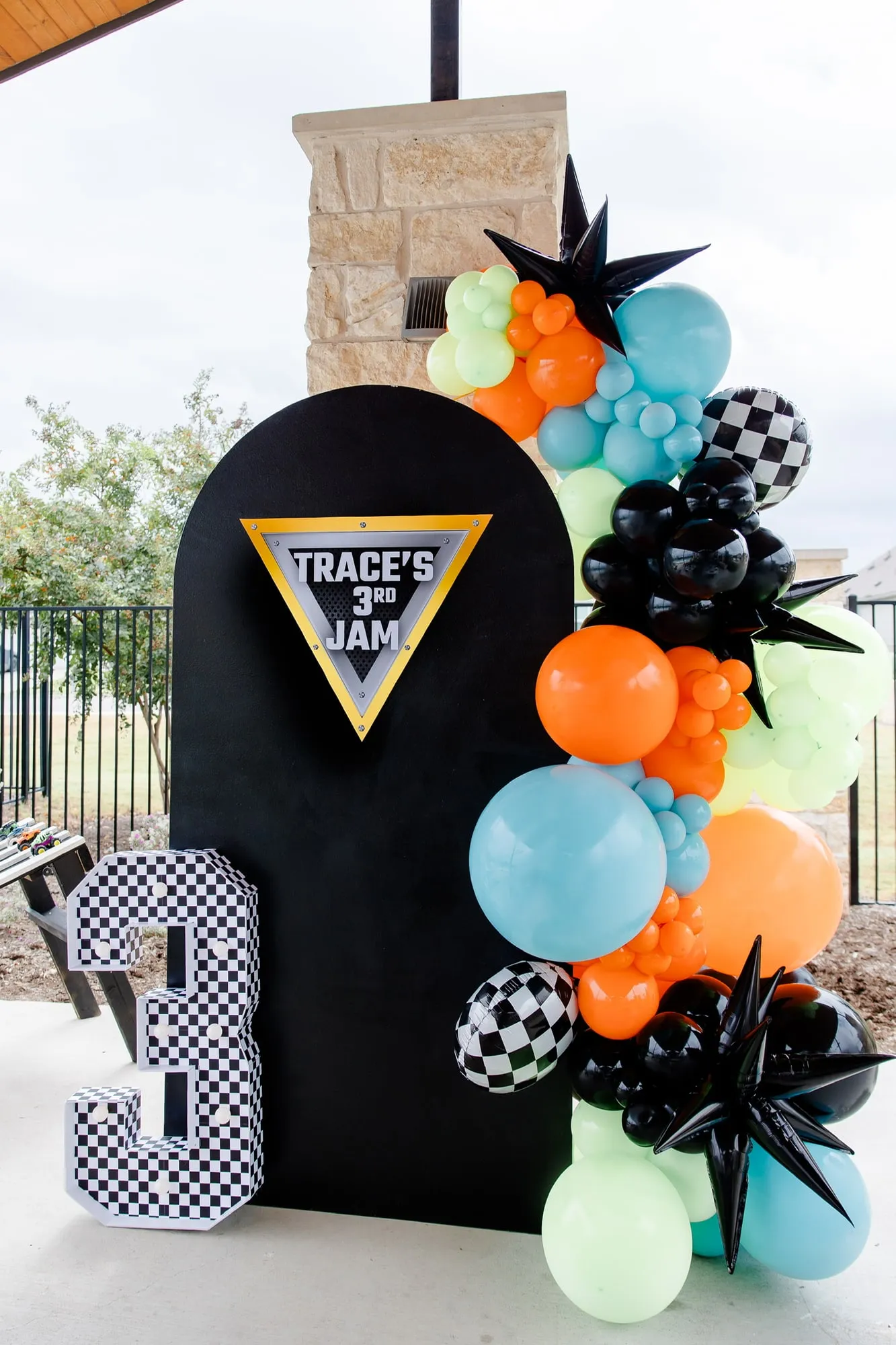 Monster truck themed third birthday with a black arch backdrop, orange, blue and lime balloon garland and a checkered number 3