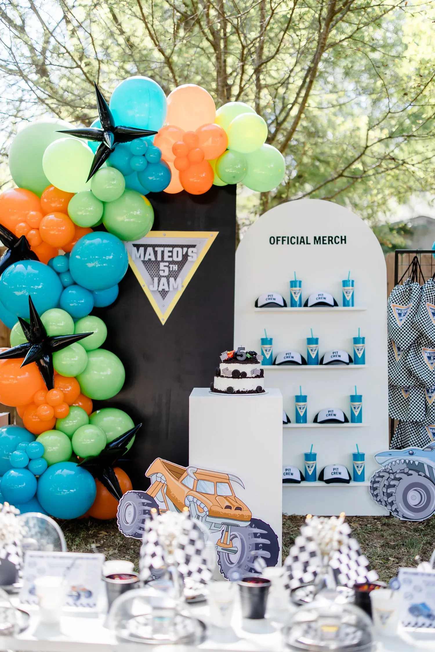 Monster truck fifth birthday with teal, orange and green balloon garland and custom merch wall