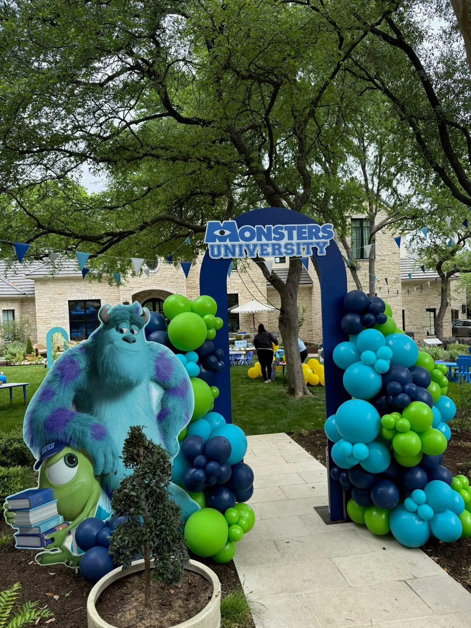 Monsters University themed entrance arch with navy, teal and lime balloon columns and pennant flags in a backyard