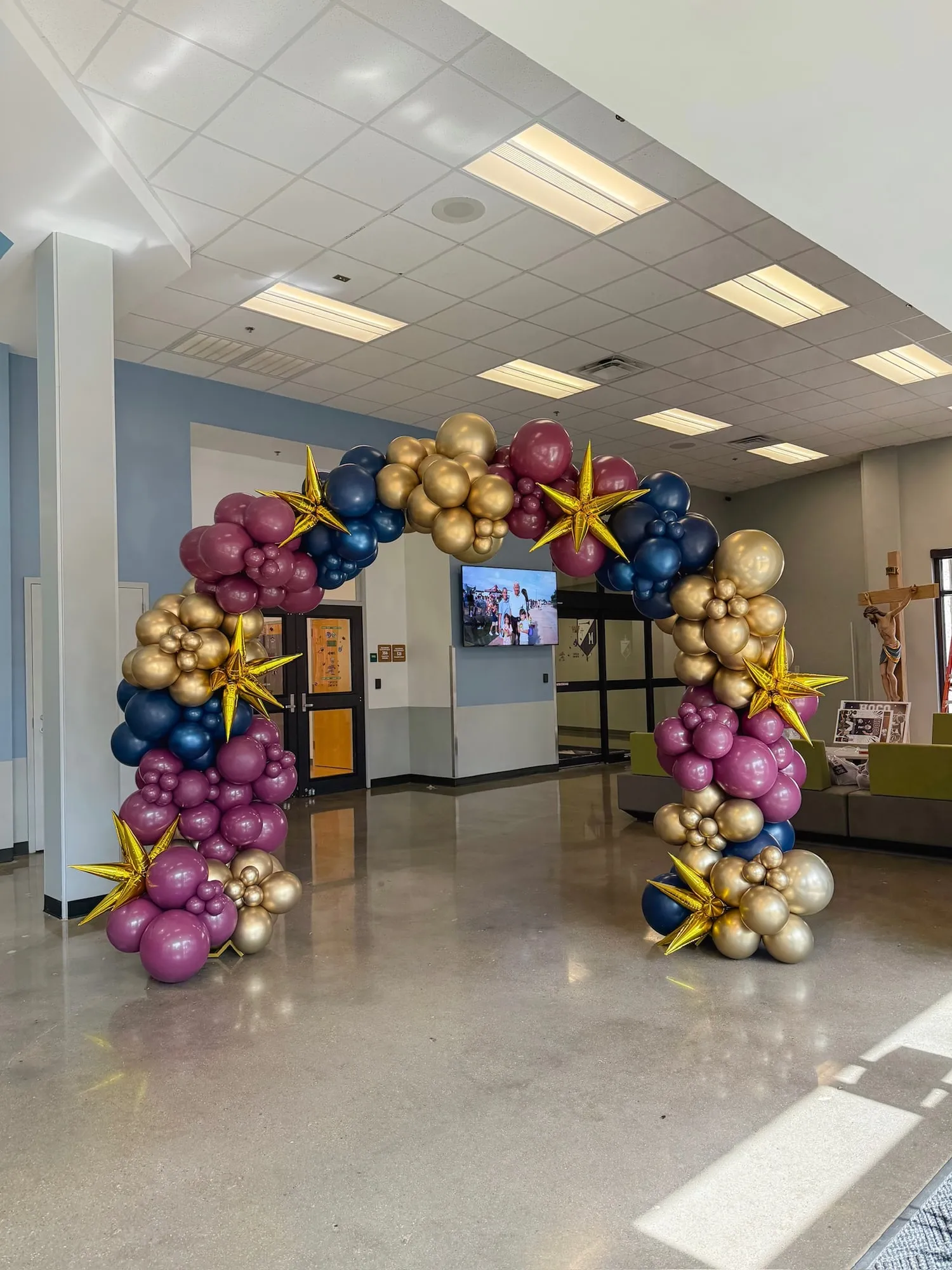 Navy, burgundy and gold balloon arch with gold starburst balloons in a school lobby