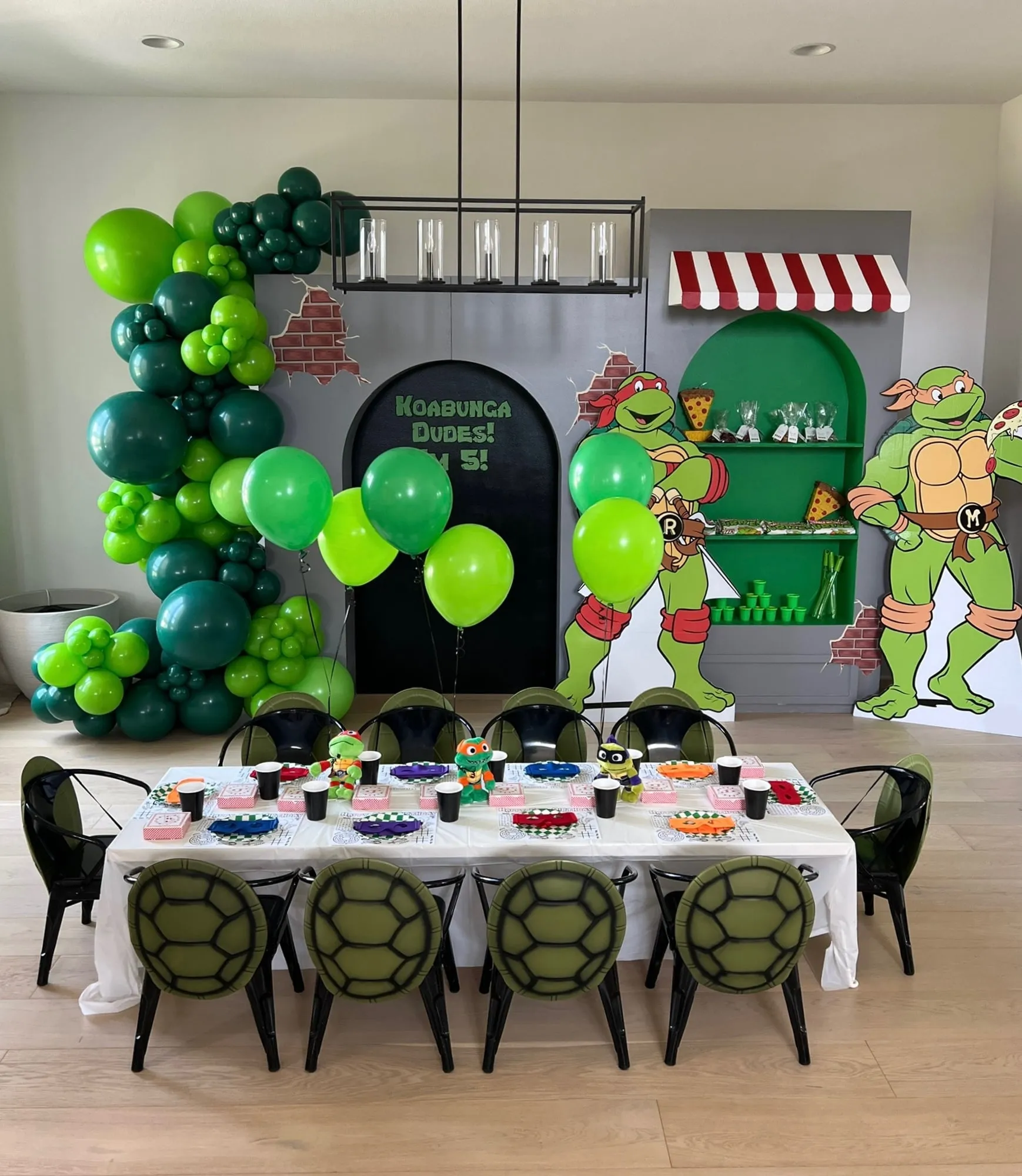 Ninja Turtles themed fifth birthday with a pizza shop backdrop, green balloon garland, turtle shell chairs and a styled kids table