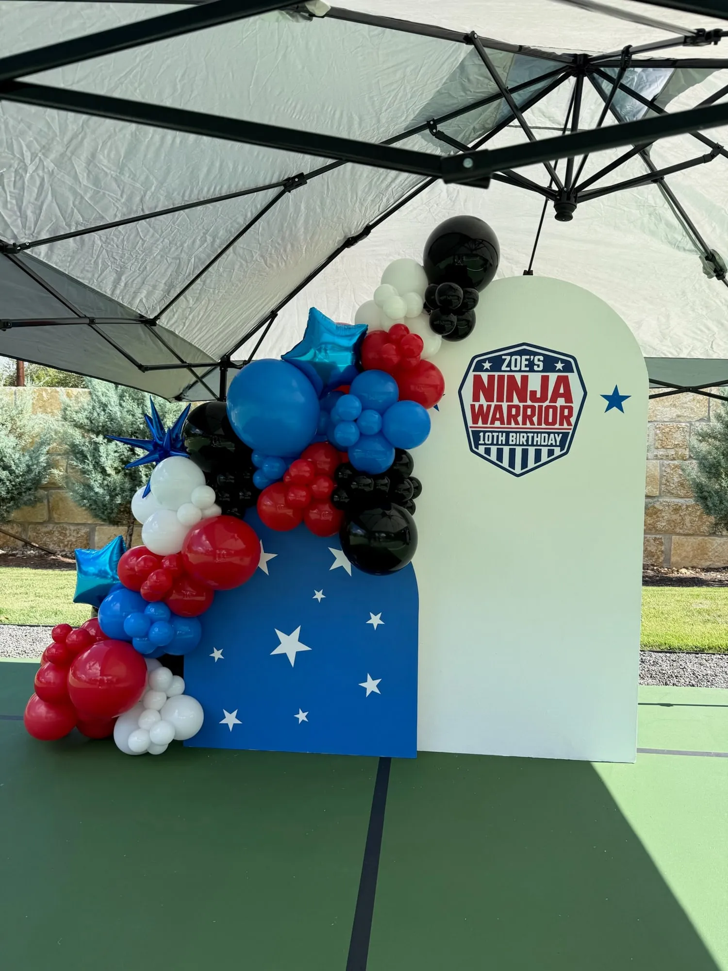 Ninja warrior tenth birthday with a white arch, blue star panel and red, white, blue and black balloon garland