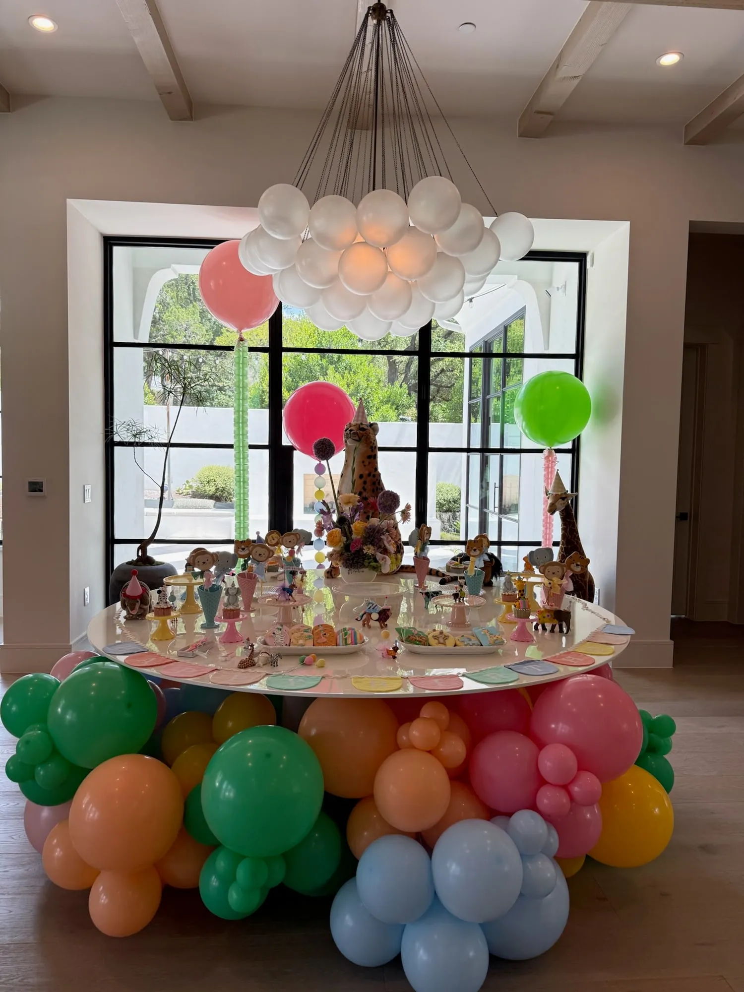 Party animals dessert table with animal treats, florals, a white balloon chandelier and a rainbow balloon base