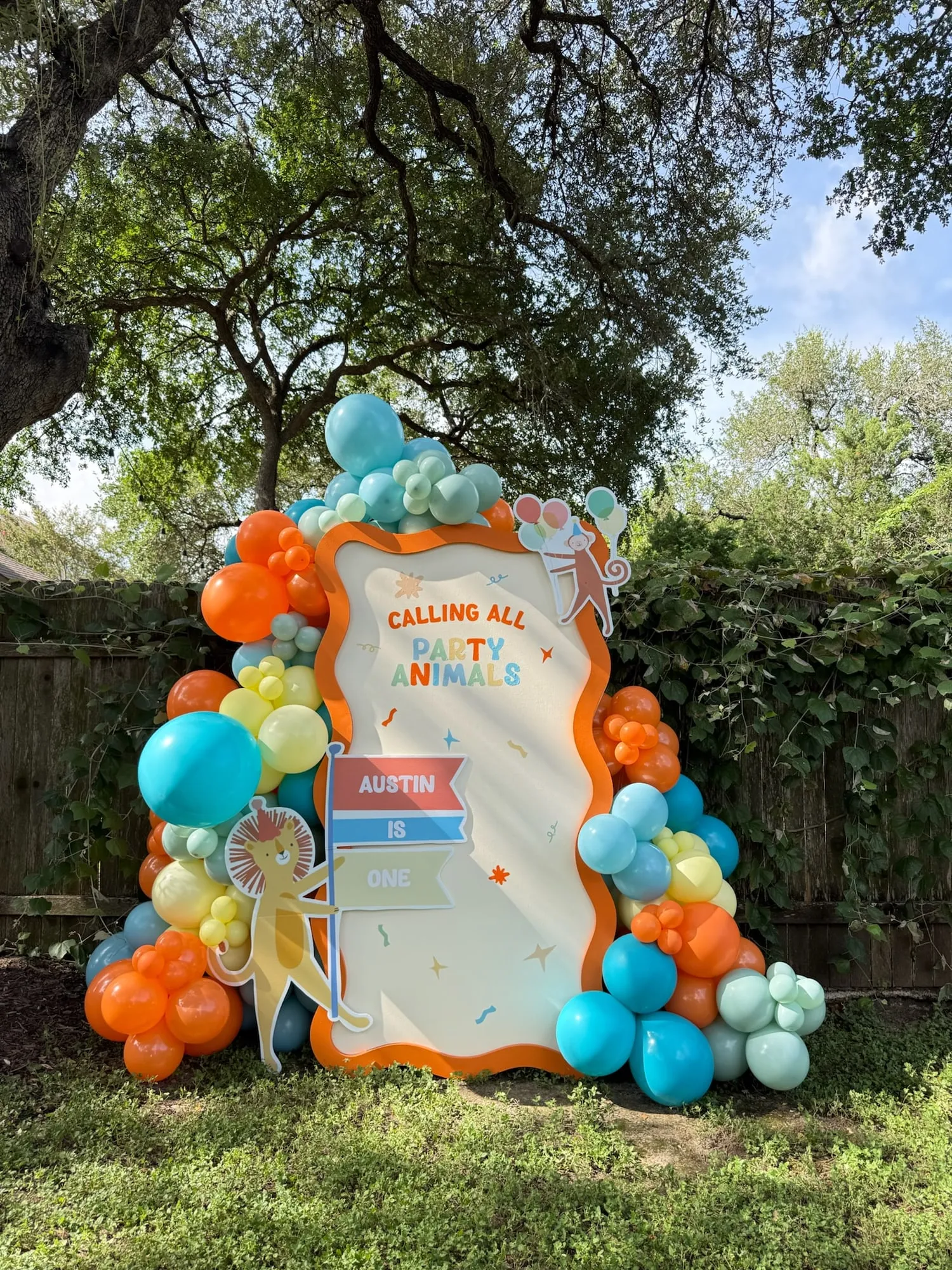 Calling All Party Animals first birthday with a wavy cream panel, lion and monkey cutouts and orange, teal and yellow balloon garland