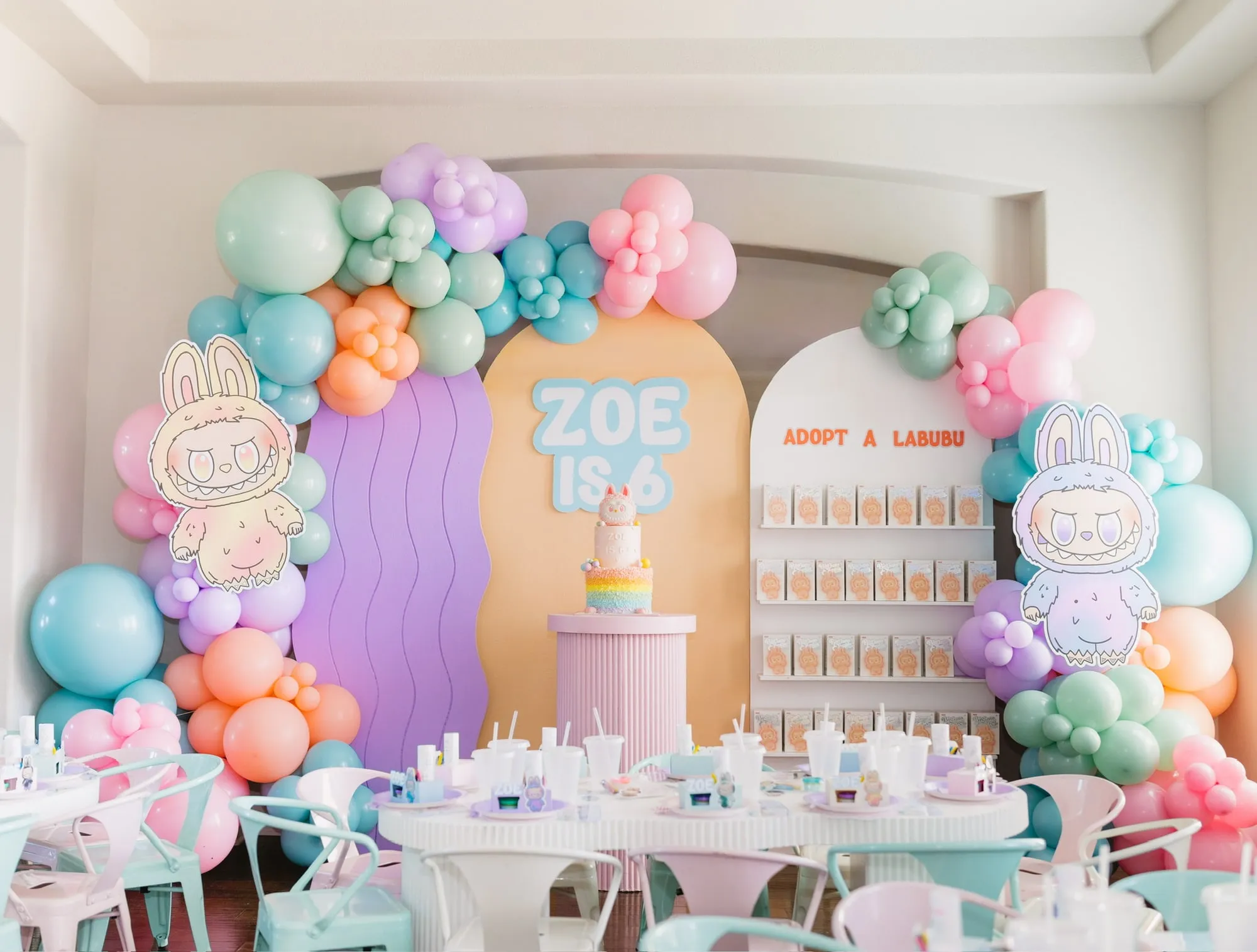 Pastel sixth birthday with purple, peach and white arches, an adopt a friend shelf, rainbow cake and styled kids tables