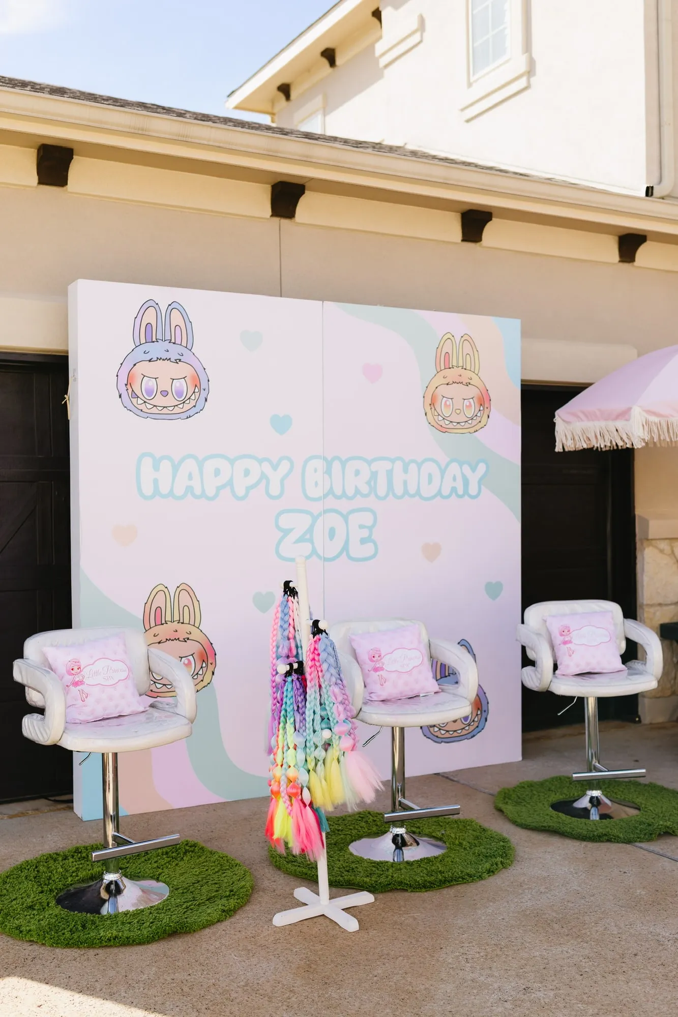 Pastel spa birthday backdrop with salon chairs, a braid station and grass mats