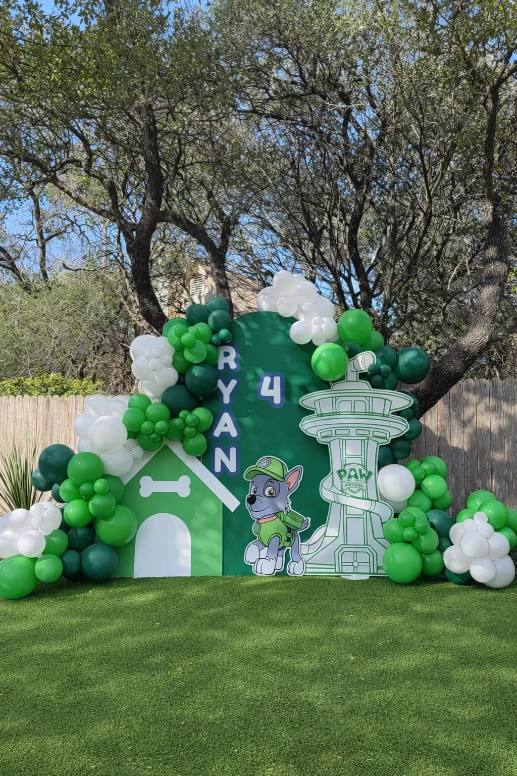 Paw Patrol themed fourth birthday with a green arch backdrop, doghouse and lookout tower cutouts and green and white balloon garland
