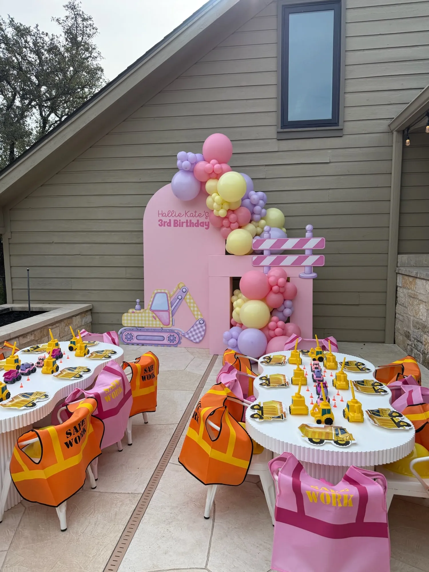 Pink construction themed third birthday with a pink arch, excavator cutout, pastel balloon garland and cloud kids tables with safety vests