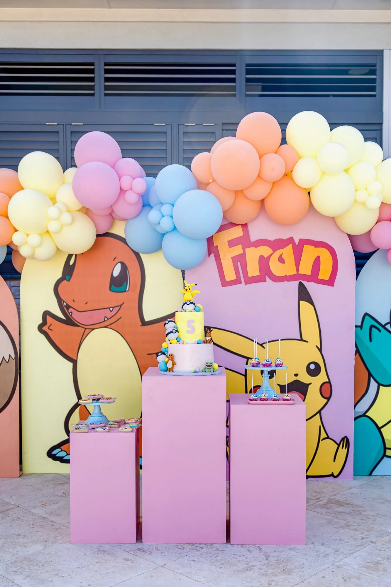 Pokemon themed fifth birthday with character arch backdrops, pastel balloon garland and pink pedestal dessert display
