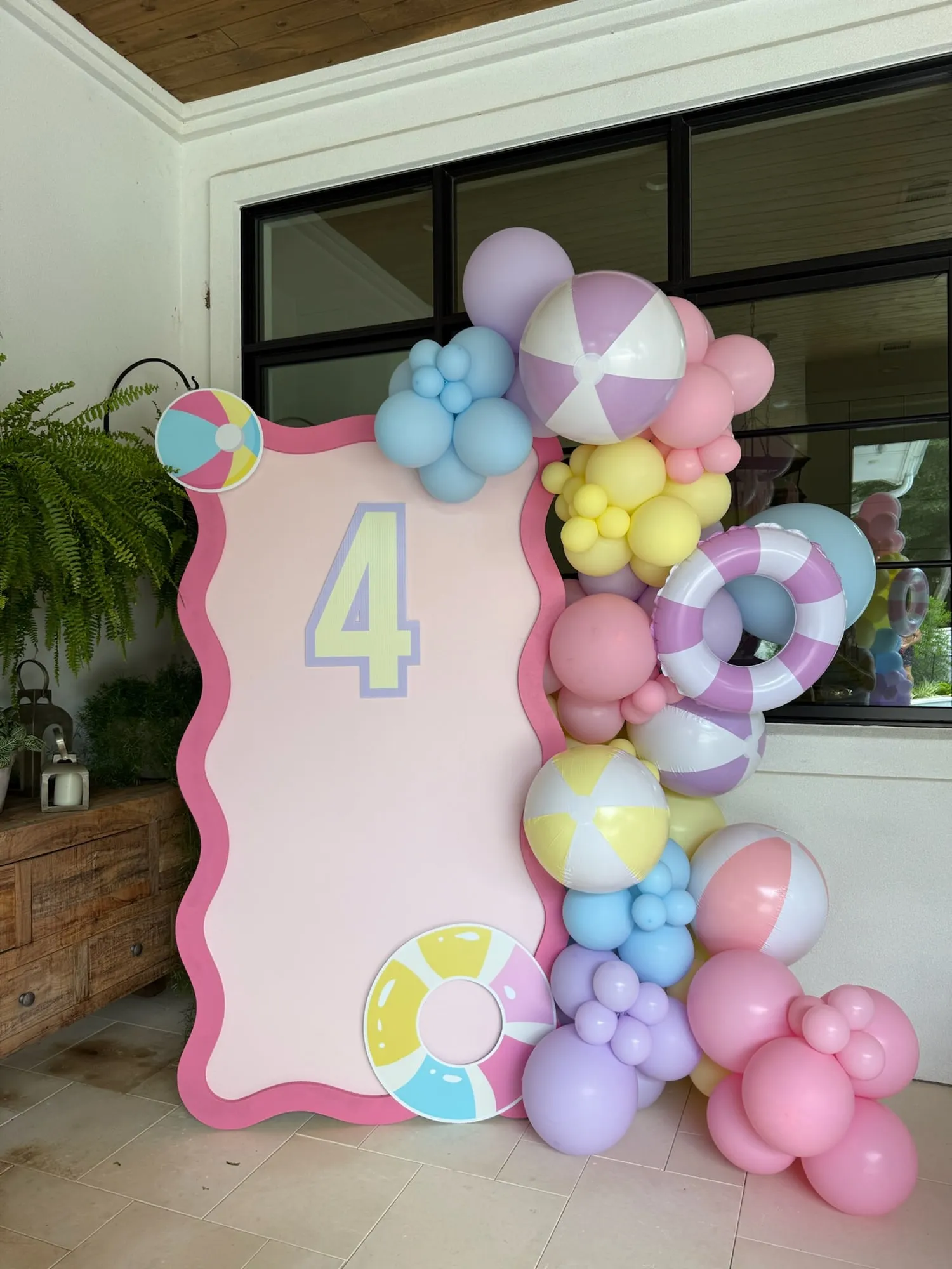 Pool party fourth birthday with a pink wavy panel and pastel balloon garland with beach balls and a pool float